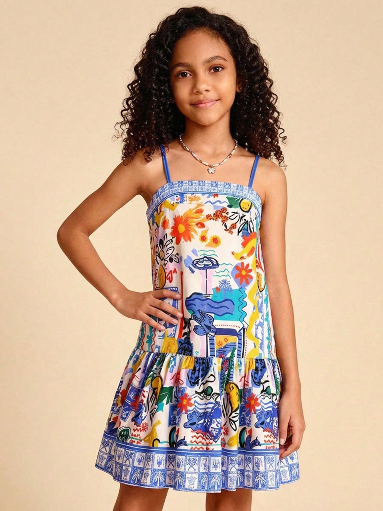 Tween girls black cami dress with colorful all-over cartoon print, spaghetti straps, ruffle detail, low waist, and flounce hem