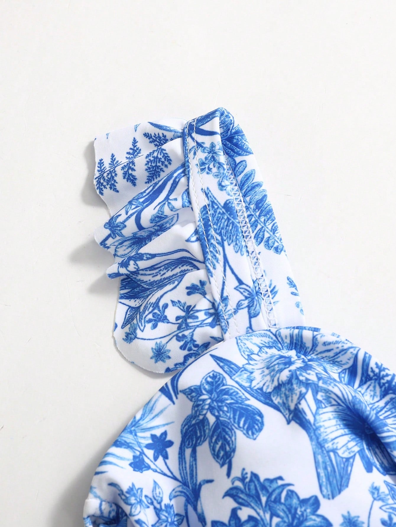 Tween girls blue and white floral print one-piece swimsuit with ruffle detail, spaghetti straps, V-neck styling, and vacation beachwear look.