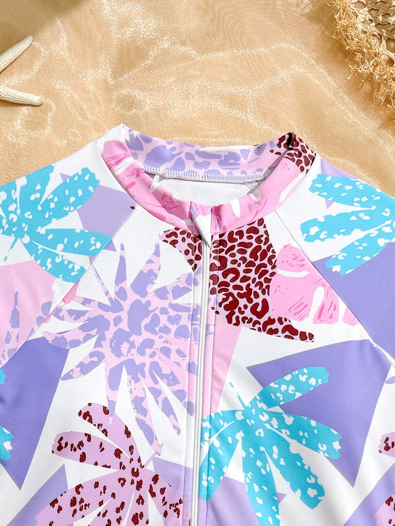 Girls one-piece swimsuit in blue with all-over leopard leaf print, ruffle detail, zipper front, high neck, and lined body for swimming and vacation.