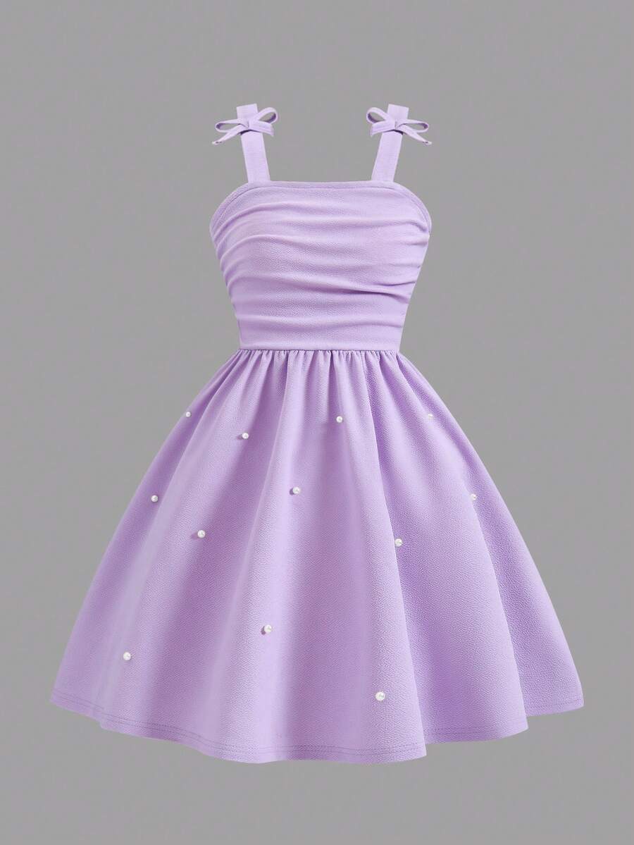 Tween girl wearing a purple sleeveless striped cami mini dress featuring a high waist flared hem and beaded pearl details.