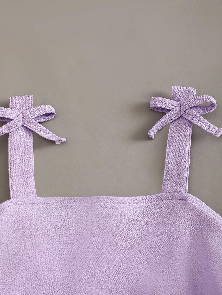 Tween girl wearing a purple sleeveless striped cami mini dress featuring a high waist flared hem and beaded pearl details.