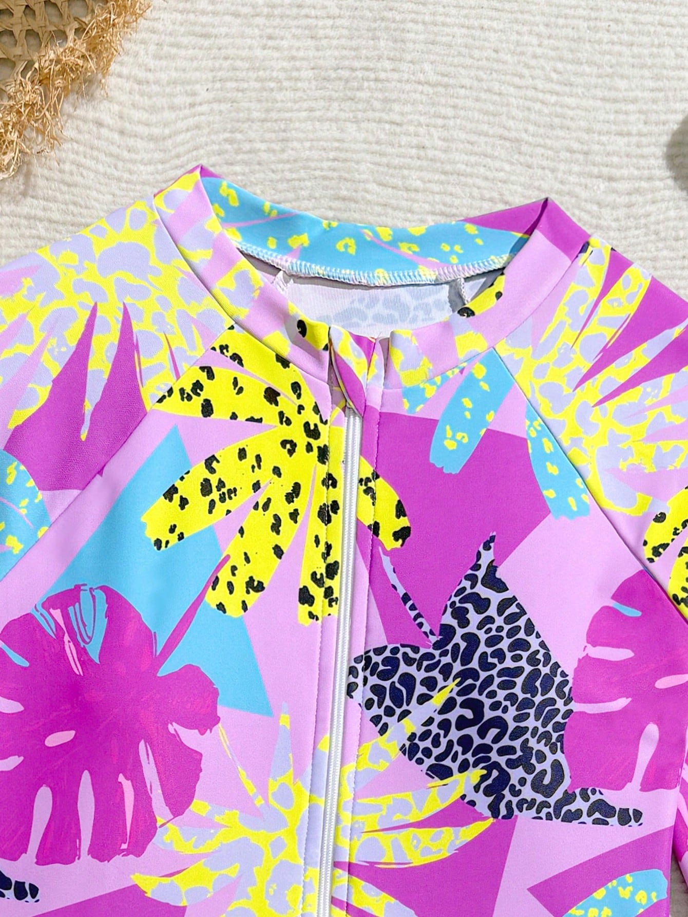 Girls one-piece swimsuit in blue with all-over leopard leaf print, ruffle detail, zipper front, high neck, and lined body for swimming and vacation.