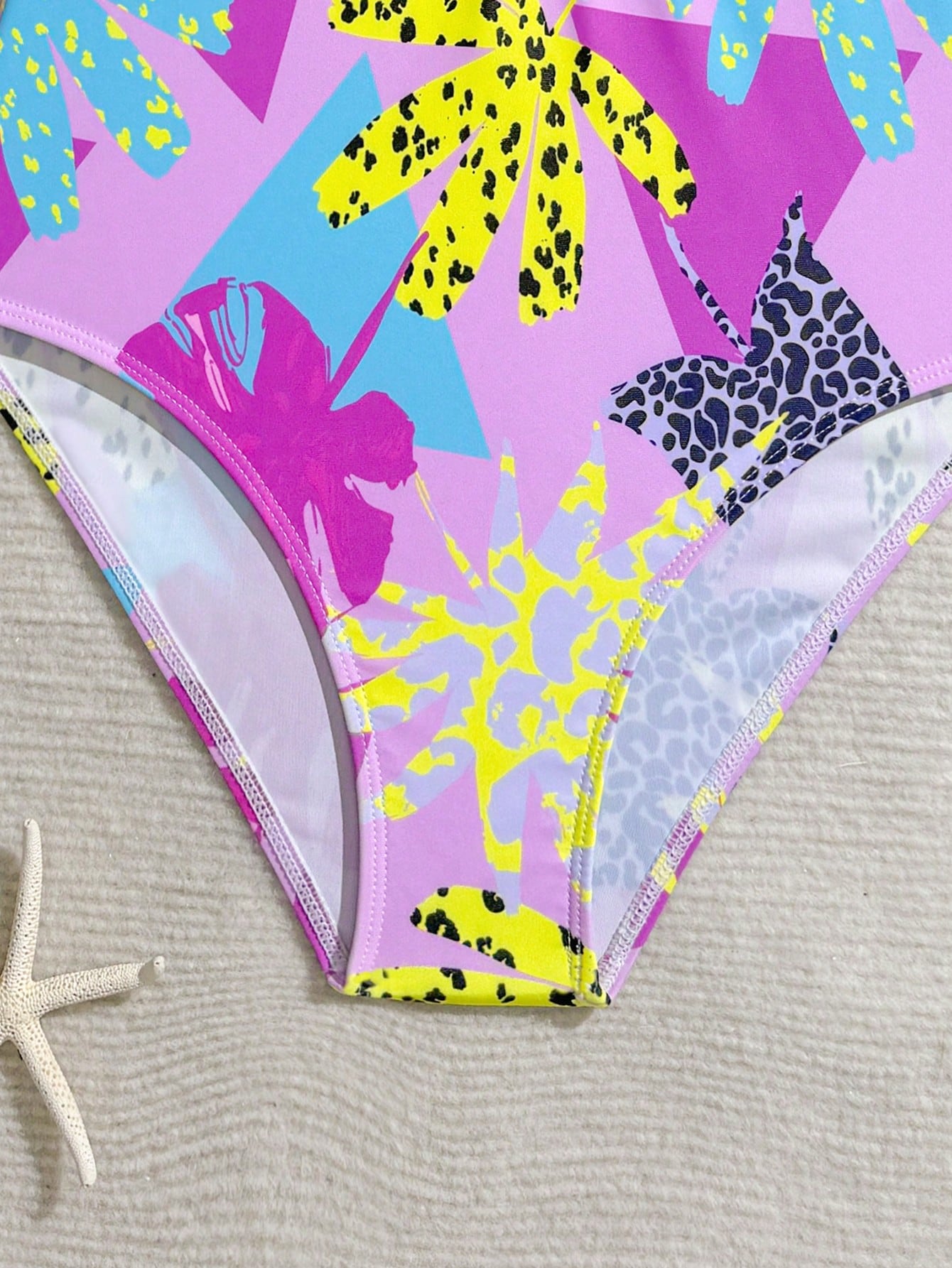 Girls one-piece swimsuit in blue with all-over leopard leaf print, ruffle detail, zipper front, high neck, and lined body for swimming and vacation.
