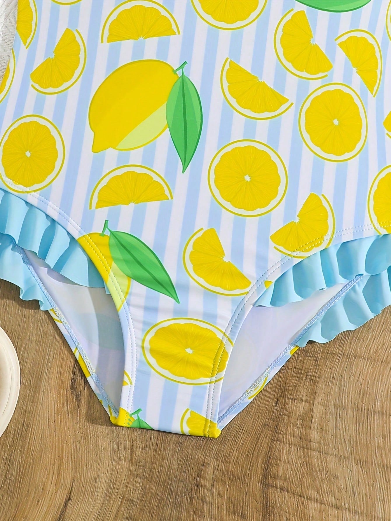 Tween girls purple one-piece swimsuit with lemon stripe pattern, spaghetti straps, ruffle detail, bow design, scoop neckline, and fitted swimwear shape