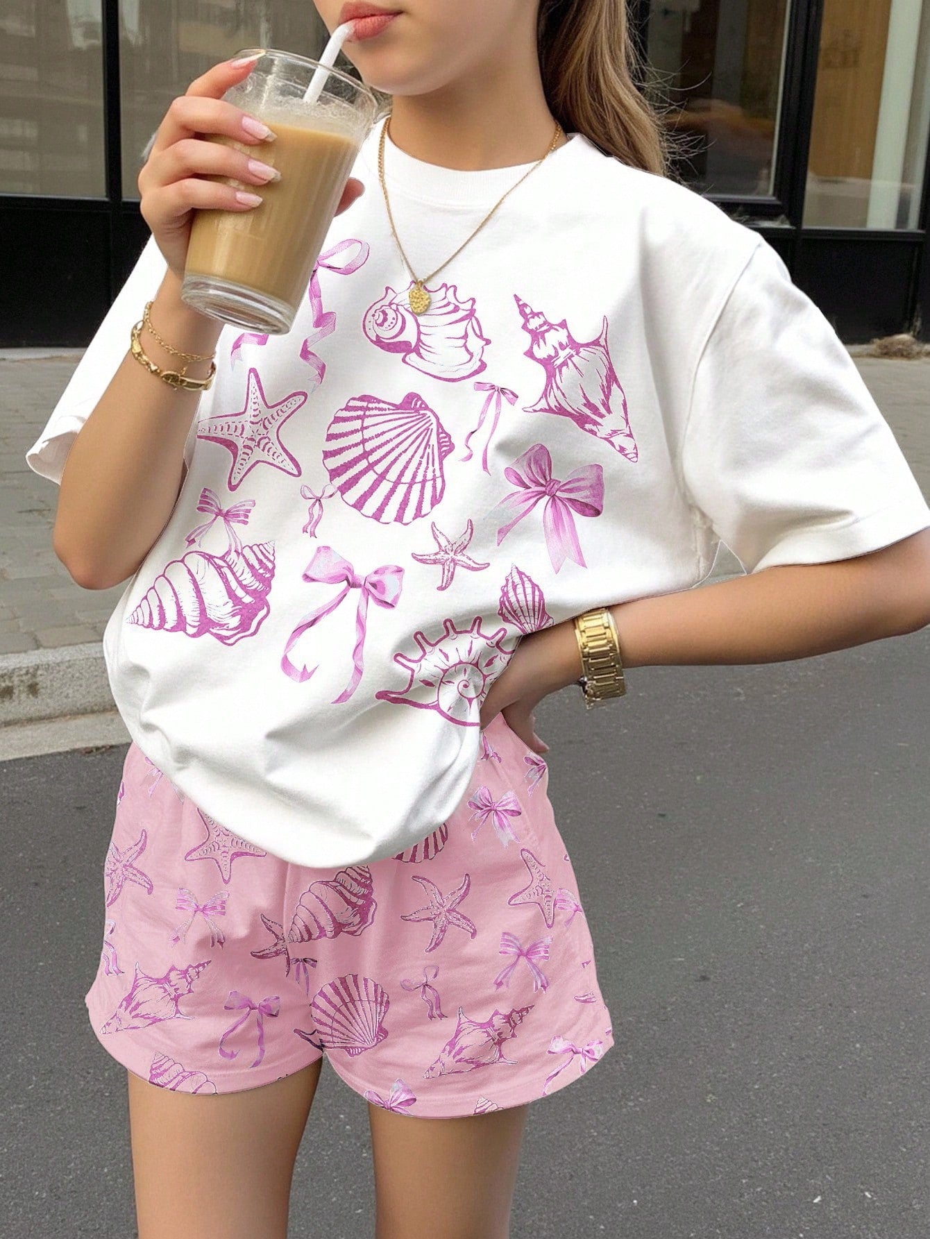 Teen girl wearing 2-piece summer vacation set with blue and white striped short sleeve top featuring seashell ocean bow print and matching loose fit shorts with pockets.