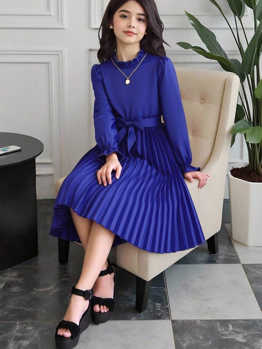 Tween girl wearing a royal blue long sleeve pleated casual A-line dress featuring a stand collar, flare sleeves, high waist with front tie belt, and ruffle hem.