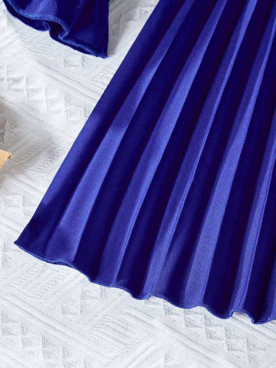 Tween girl wearing a royal blue long sleeve pleated casual A-line dress featuring a stand collar, flare sleeves, high waist with front tie belt, and ruffle hem.