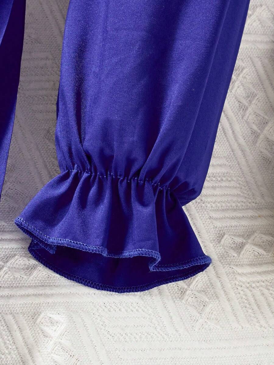 Tween girl wearing a royal blue long sleeve pleated casual A-line dress featuring a stand collar, flare sleeves, high waist with front tie belt, and ruffle hem.