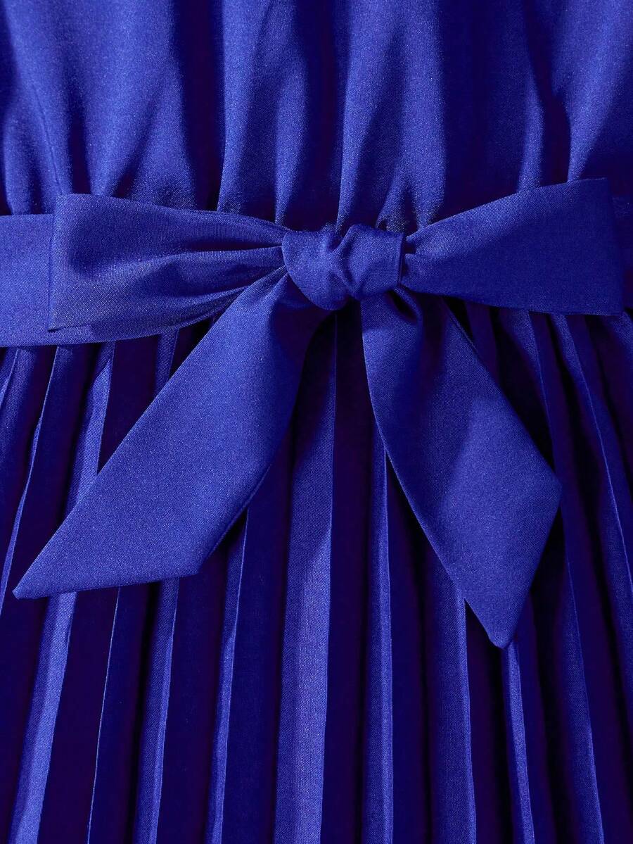 Tween girl wearing a royal blue long sleeve pleated casual A-line dress featuring a stand collar, flare sleeves, high waist with front tie belt, and ruffle hem.