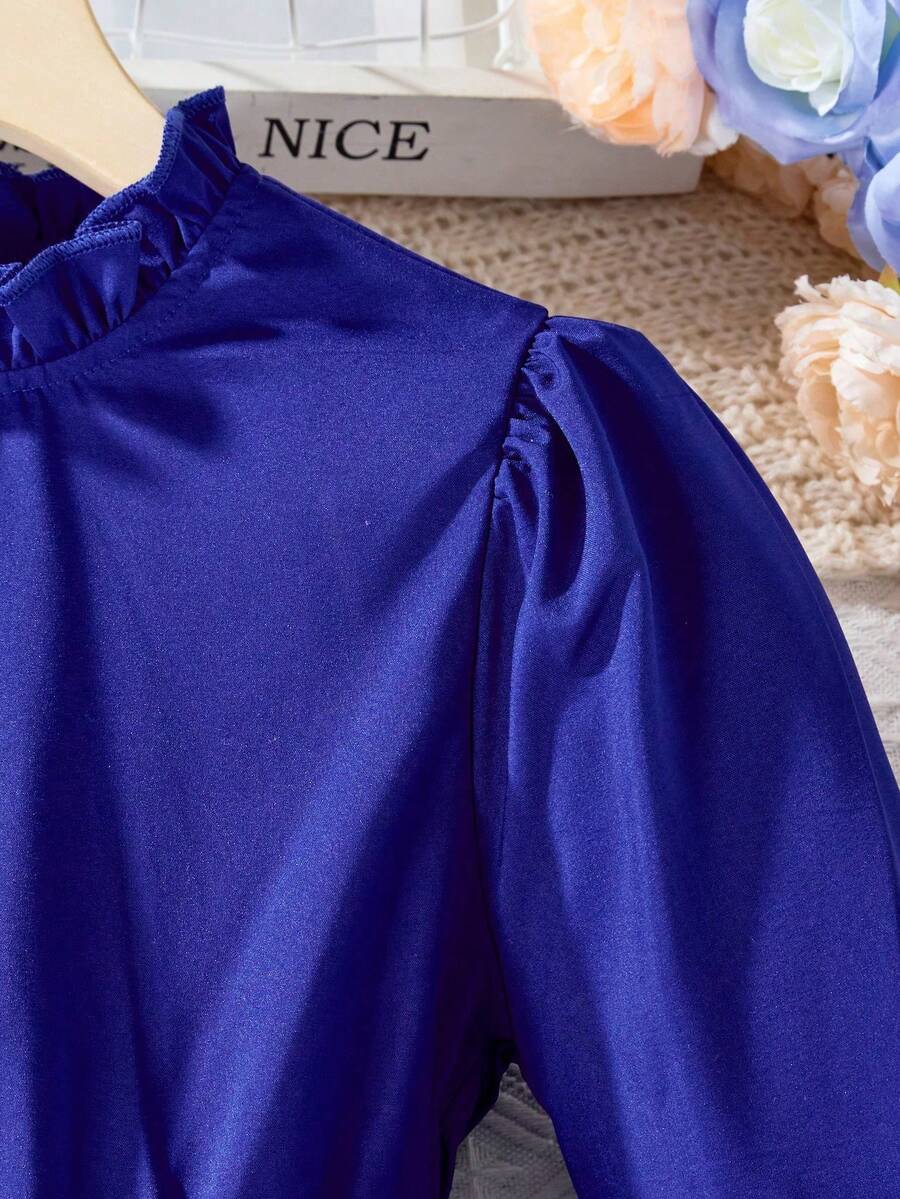 Tween girl wearing a royal blue long sleeve pleated casual A-line dress featuring a stand collar, flare sleeves, high waist with front tie belt, and ruffle hem.