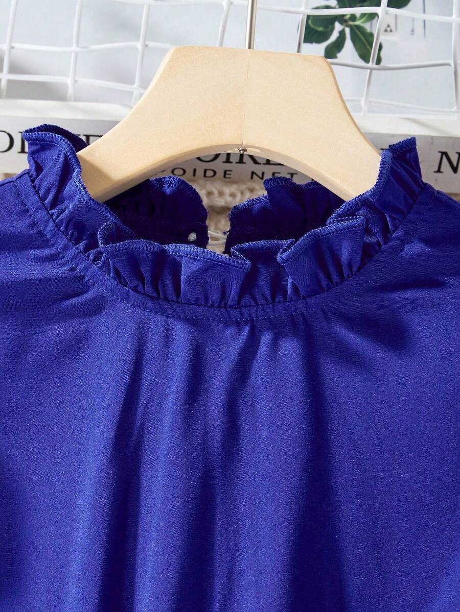 Tween girl wearing a royal blue long sleeve pleated casual A-line dress featuring a stand collar, flare sleeves, high waist with front tie belt, and ruffle hem.