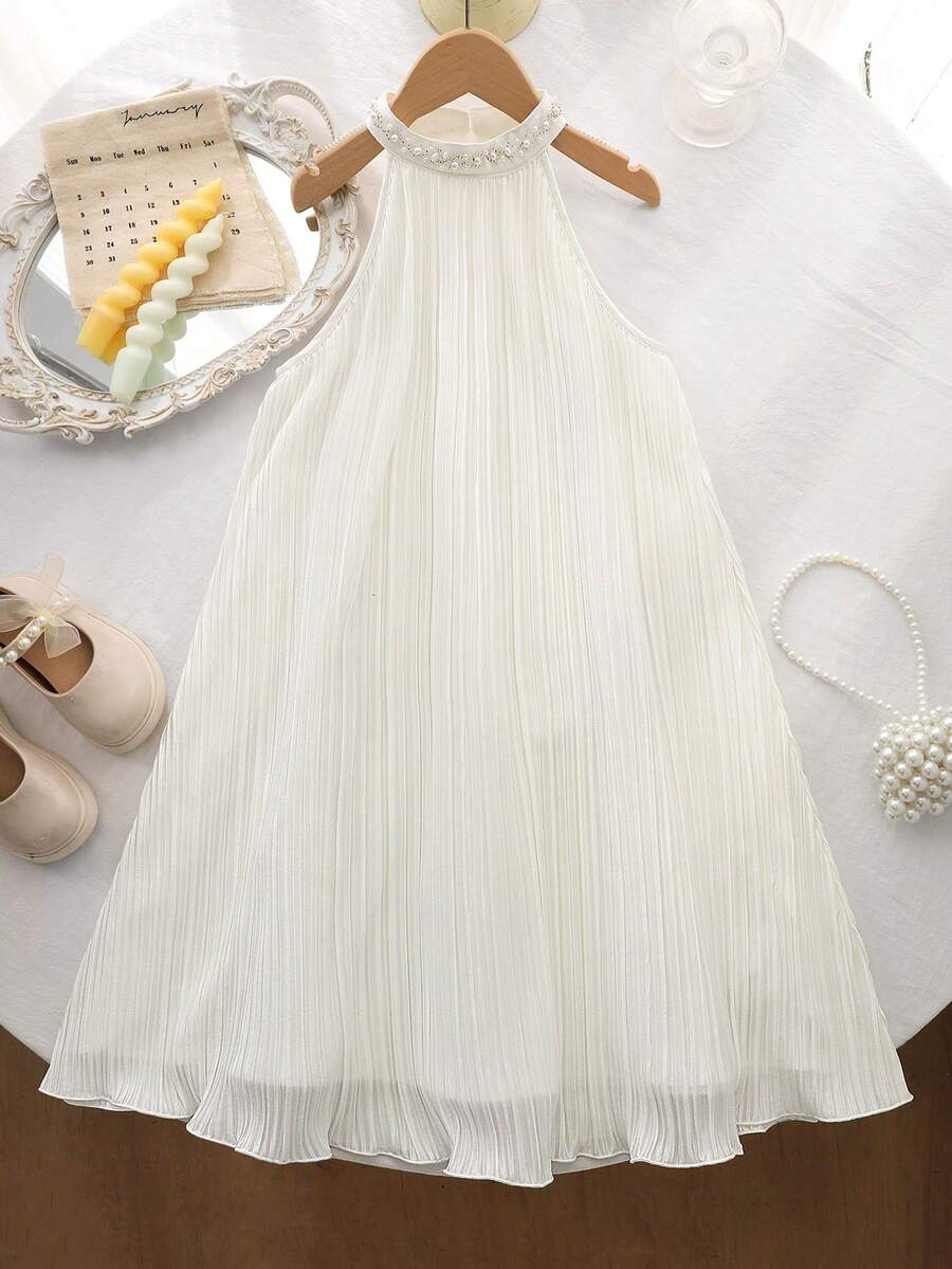 Tween girl wearing a white sleeveless pleated A-line short dress featuring a round neckline and button detail.