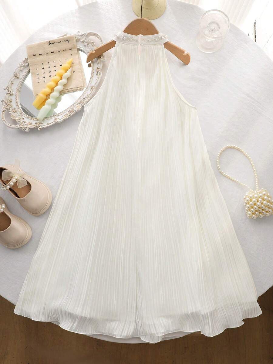 Tween girl wearing a white sleeveless pleated A-line short dress featuring a round neckline and button detail.