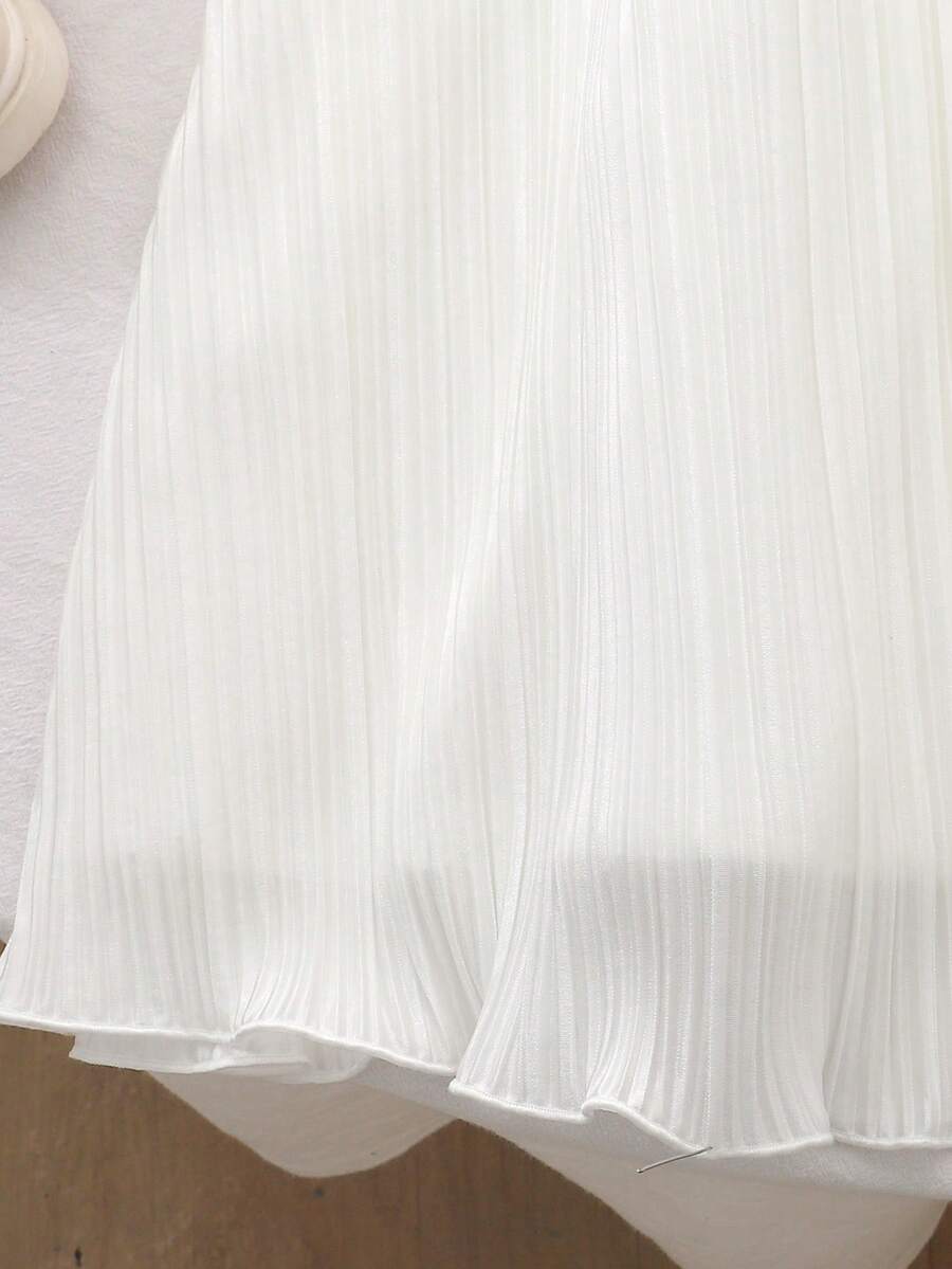 Tween girl wearing a white sleeveless pleated A-line short dress featuring a round neckline and button detail.
