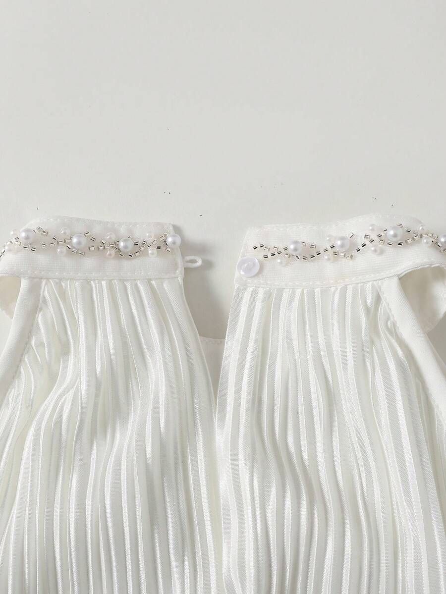Tween girl wearing a white sleeveless pleated A-line short dress featuring a round neckline and button detail.