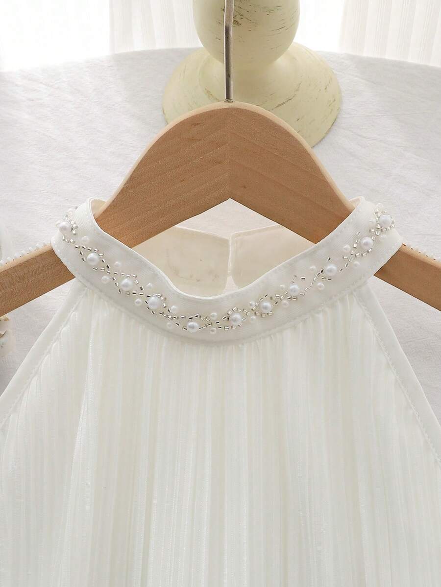 Tween girl wearing a white sleeveless pleated A-line short dress featuring a round neckline and button detail.