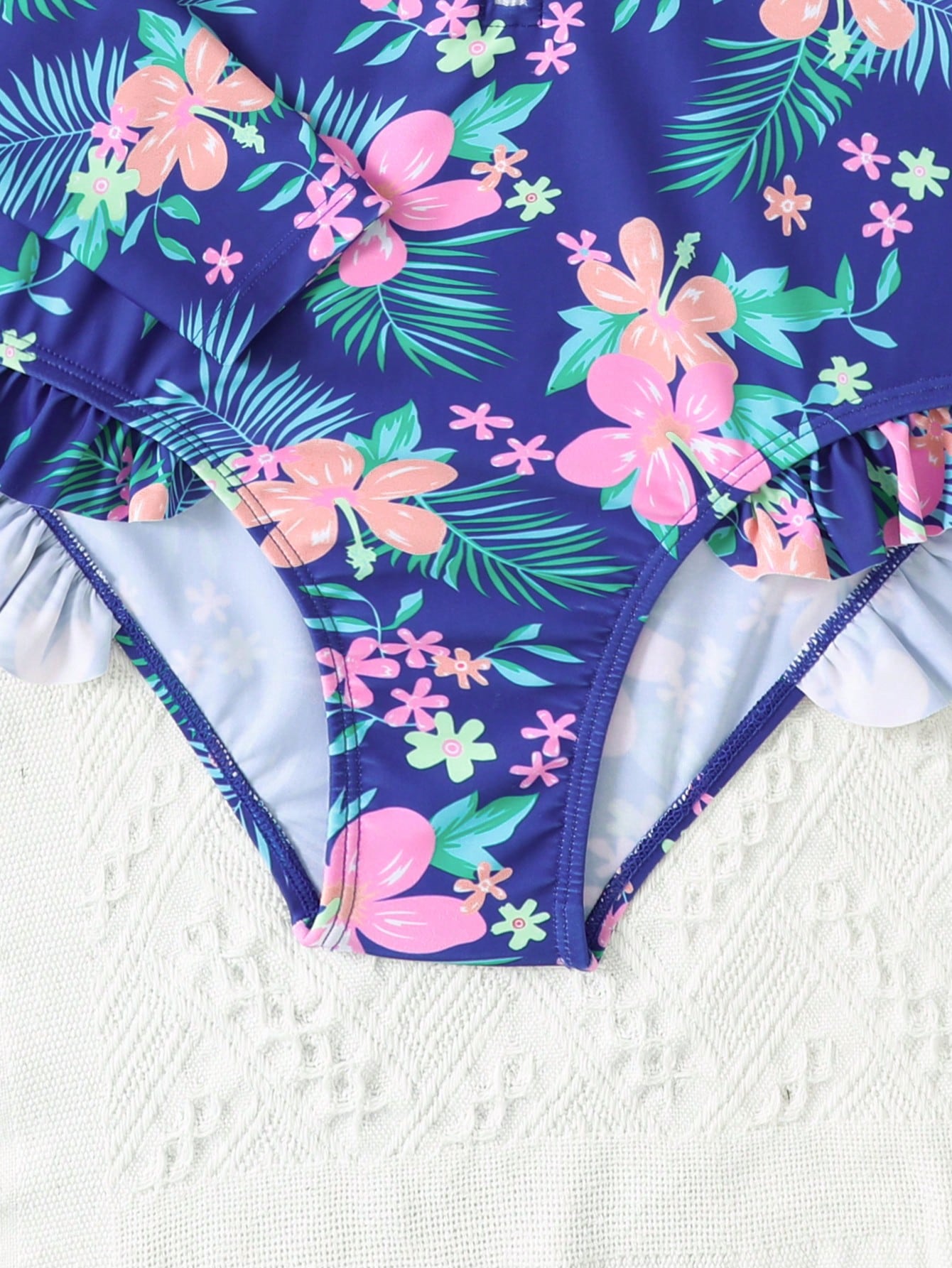 Girls one-piece swimsuit in blue with all-over leopard leaf print, ruffle detail, zipper front, high neck, and lined body for swimming and vacation.