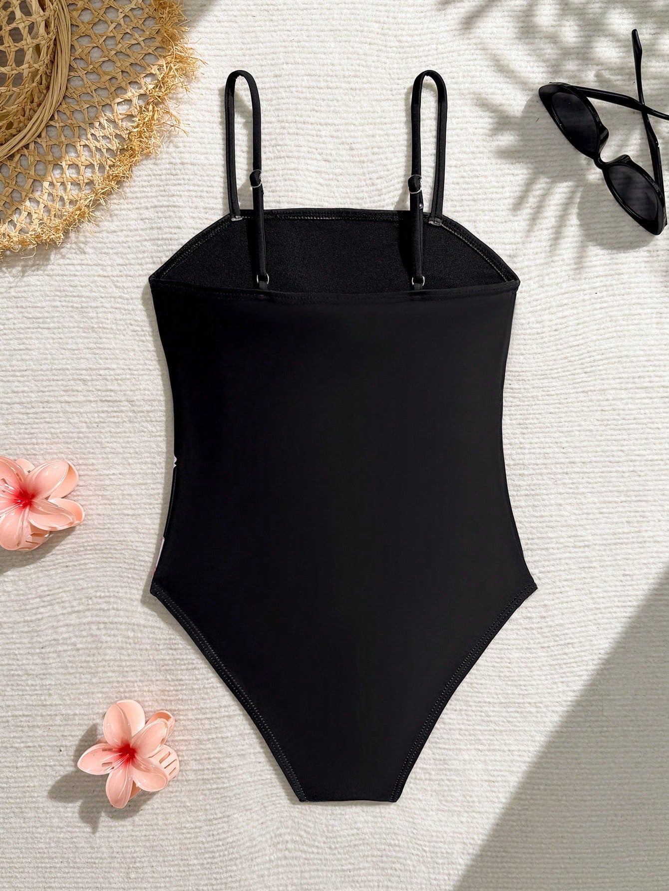 Tween girls one-piece swimsuit with a floral plant print, spaghetti straps, and a mid-waist fit in black.