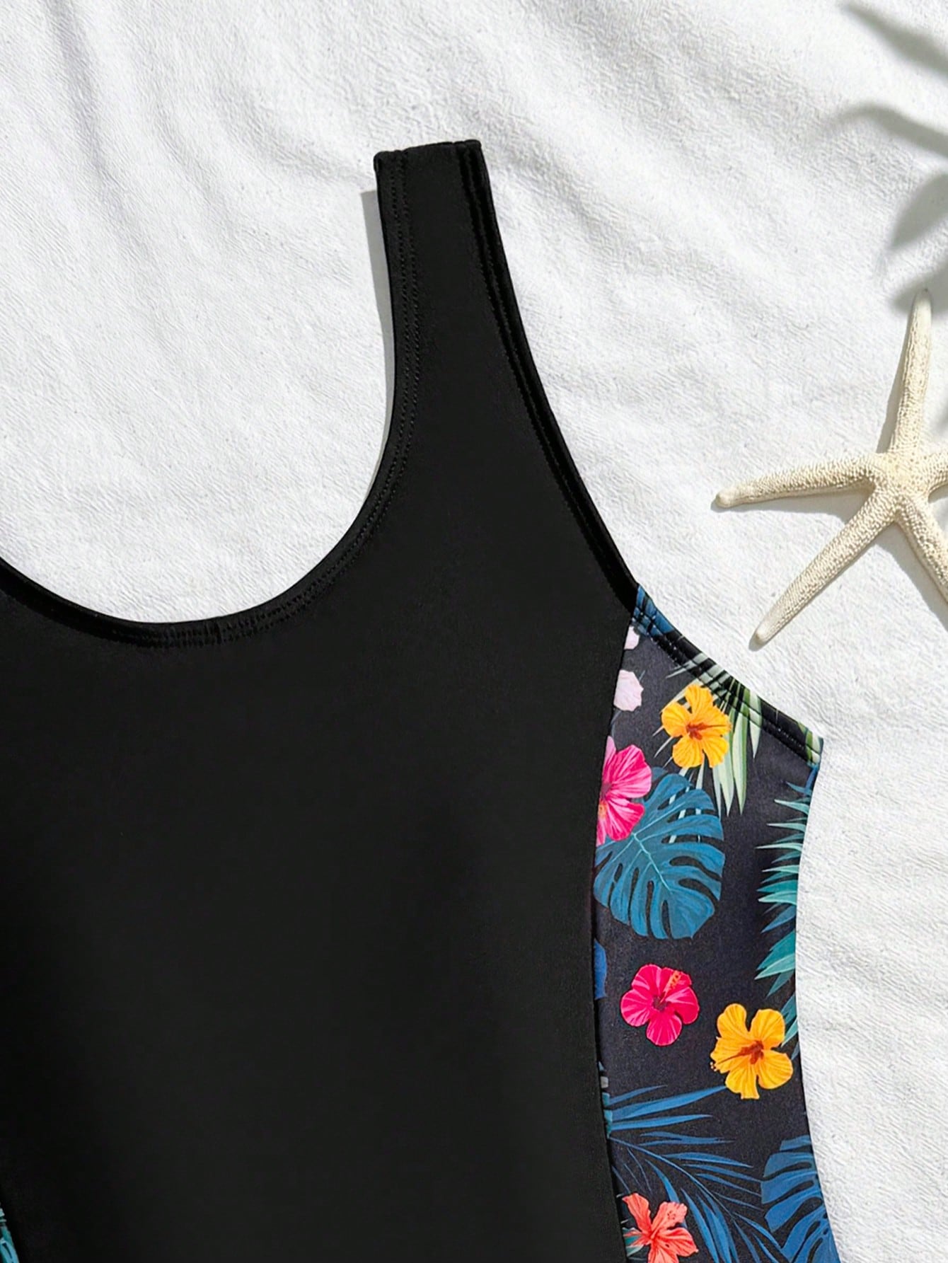 Tween girls 2-piece swimsuit set in black with full floral and plant print, featuring a sleeveless scoop-neck swim top and matching shorts-style bottoms.