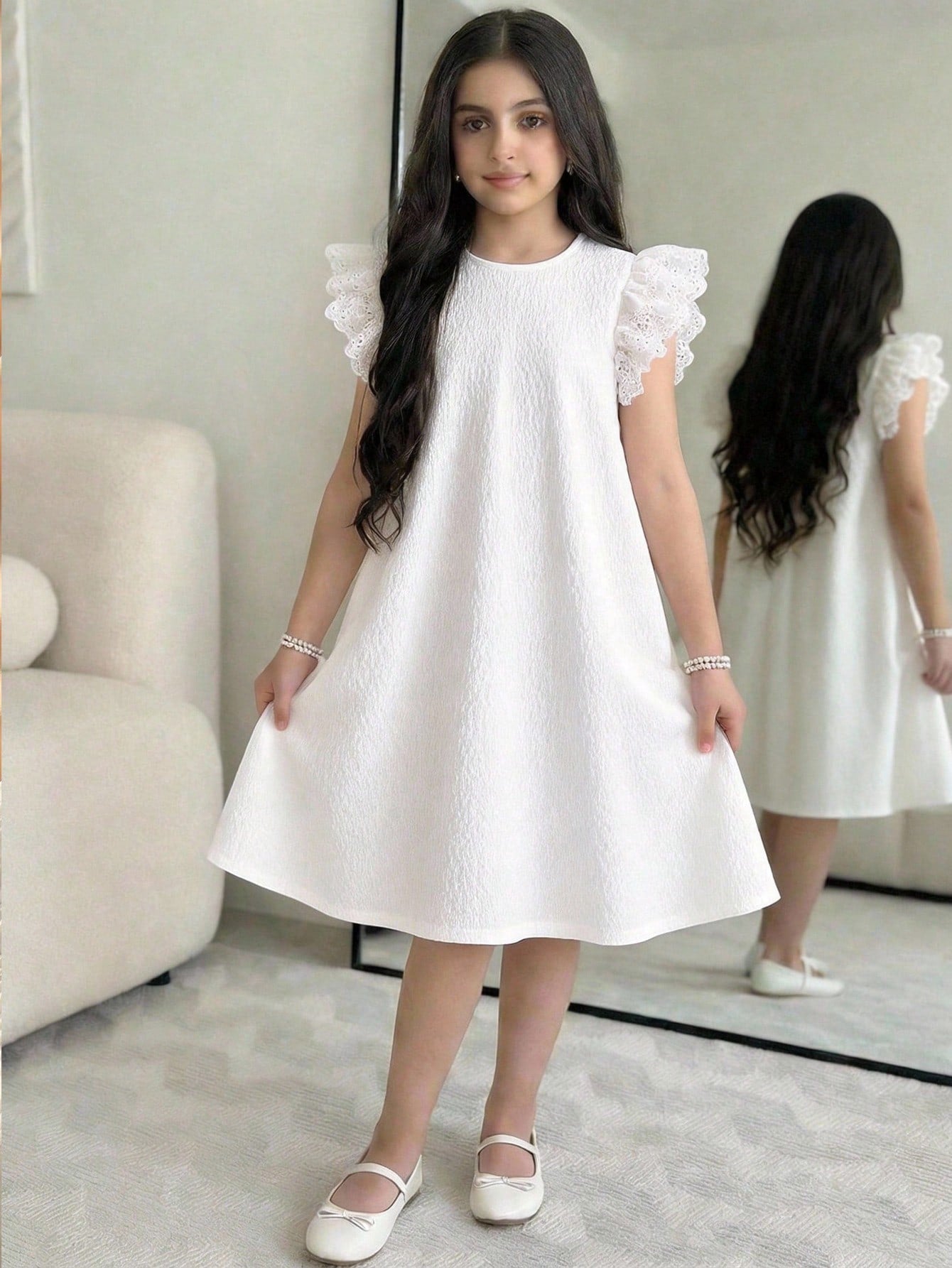 Tween girl wearing a sleeveless black tunic dress featuring a round neck, contrast lace details, and a straight hem.