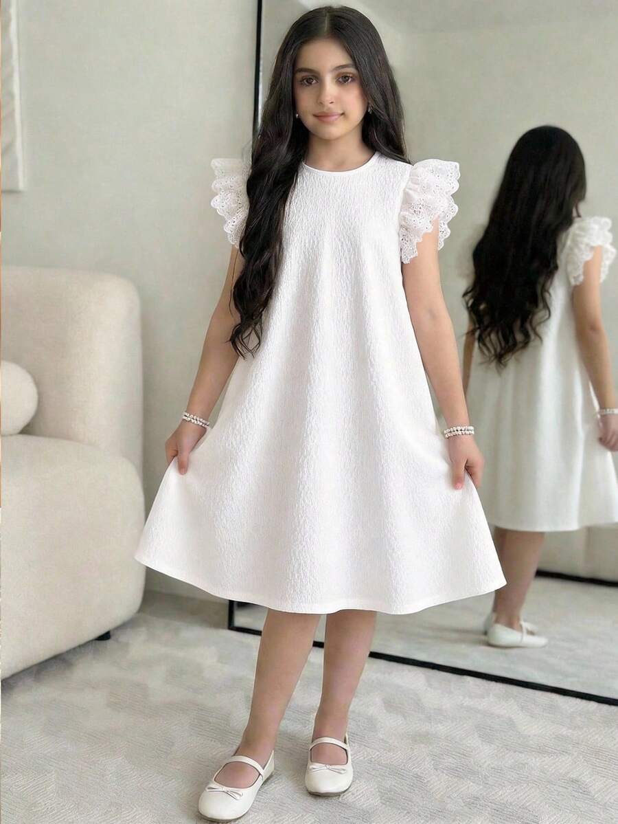 Tween girl wearing a sleeveless black tunic dress featuring a round neck, contrast lace details, and a straight hem.
