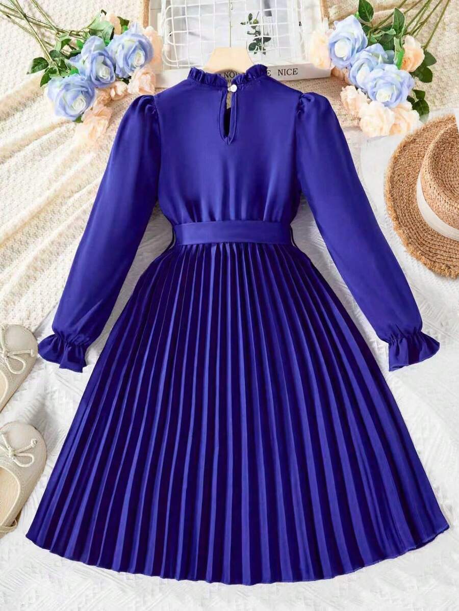 Tween girl wearing a royal blue long sleeve pleated casual A-line dress featuring a stand collar, flare sleeves, high waist with front tie belt, and ruffle hem.