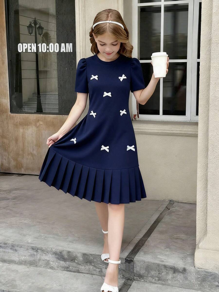 Tween girls apricot short-sleeve pleated smock dress with 3D bow decor and round neckline.