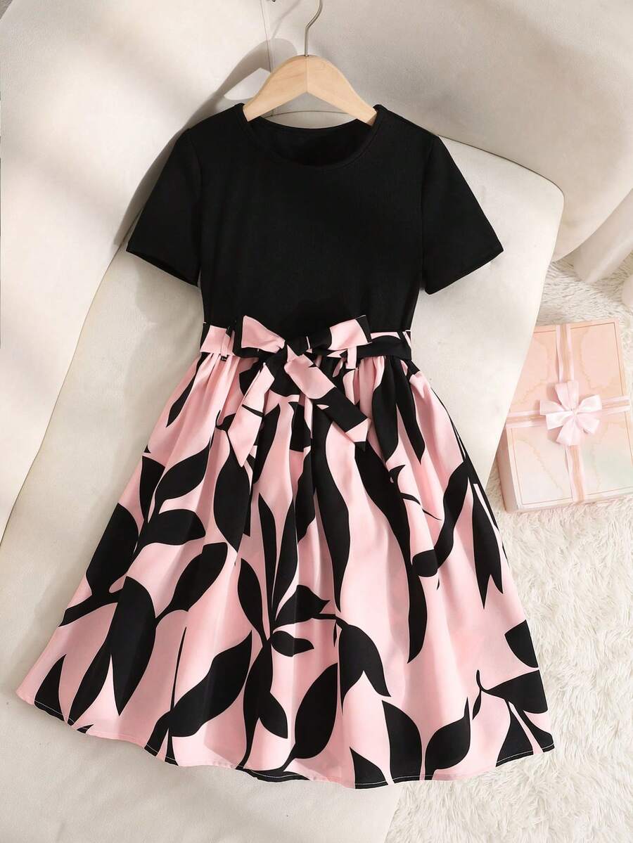 Tween girl wearing an apricot short sleeve A-line dress featuring a round neck, high waist with a belt, and flared hem.