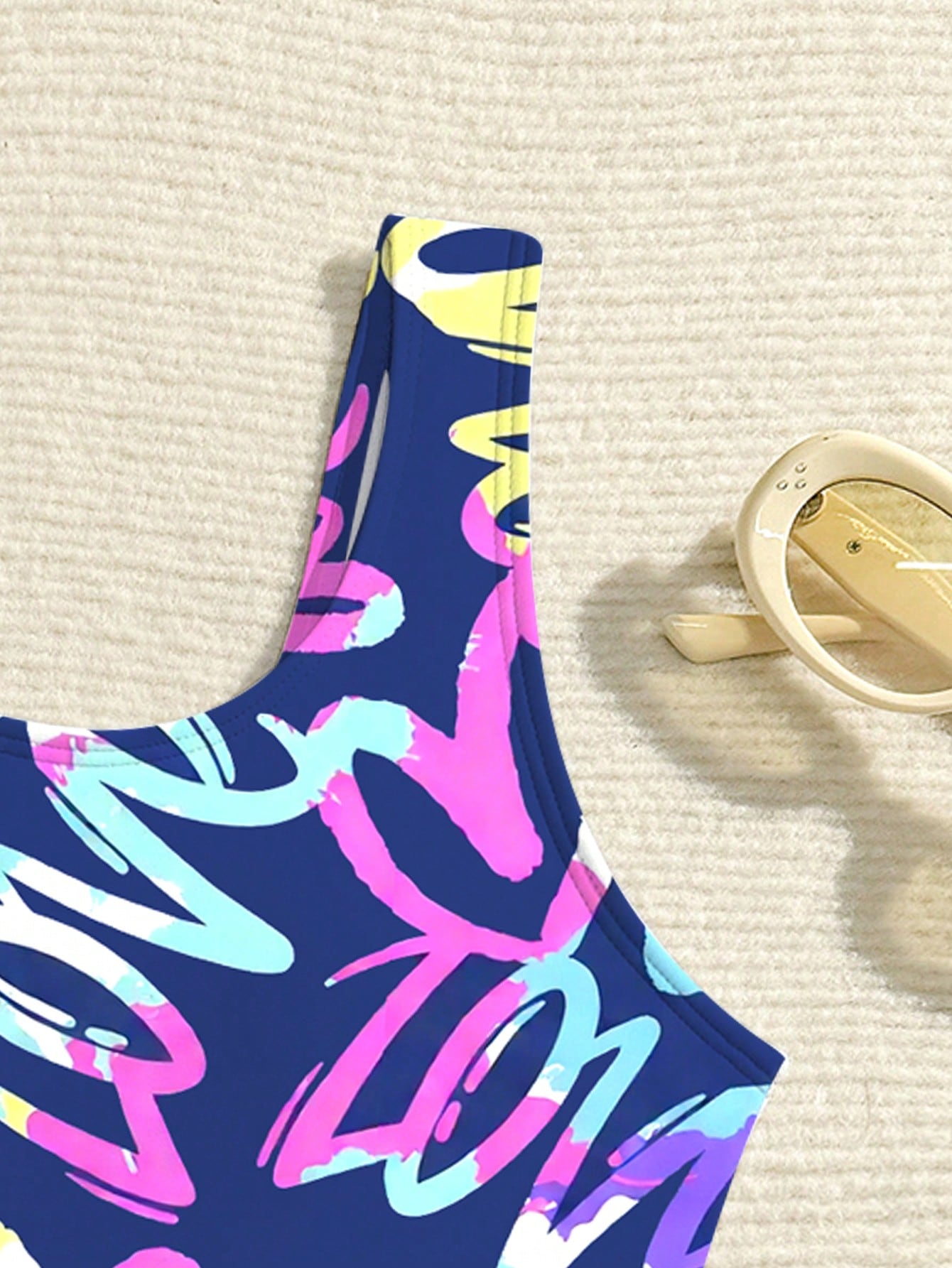 Tween girls one-piece swimsuit with a black base and multicolor tropical plant print featuring bamboo, palm leaves, plumeria flowers, scoop neck, and wide straps.