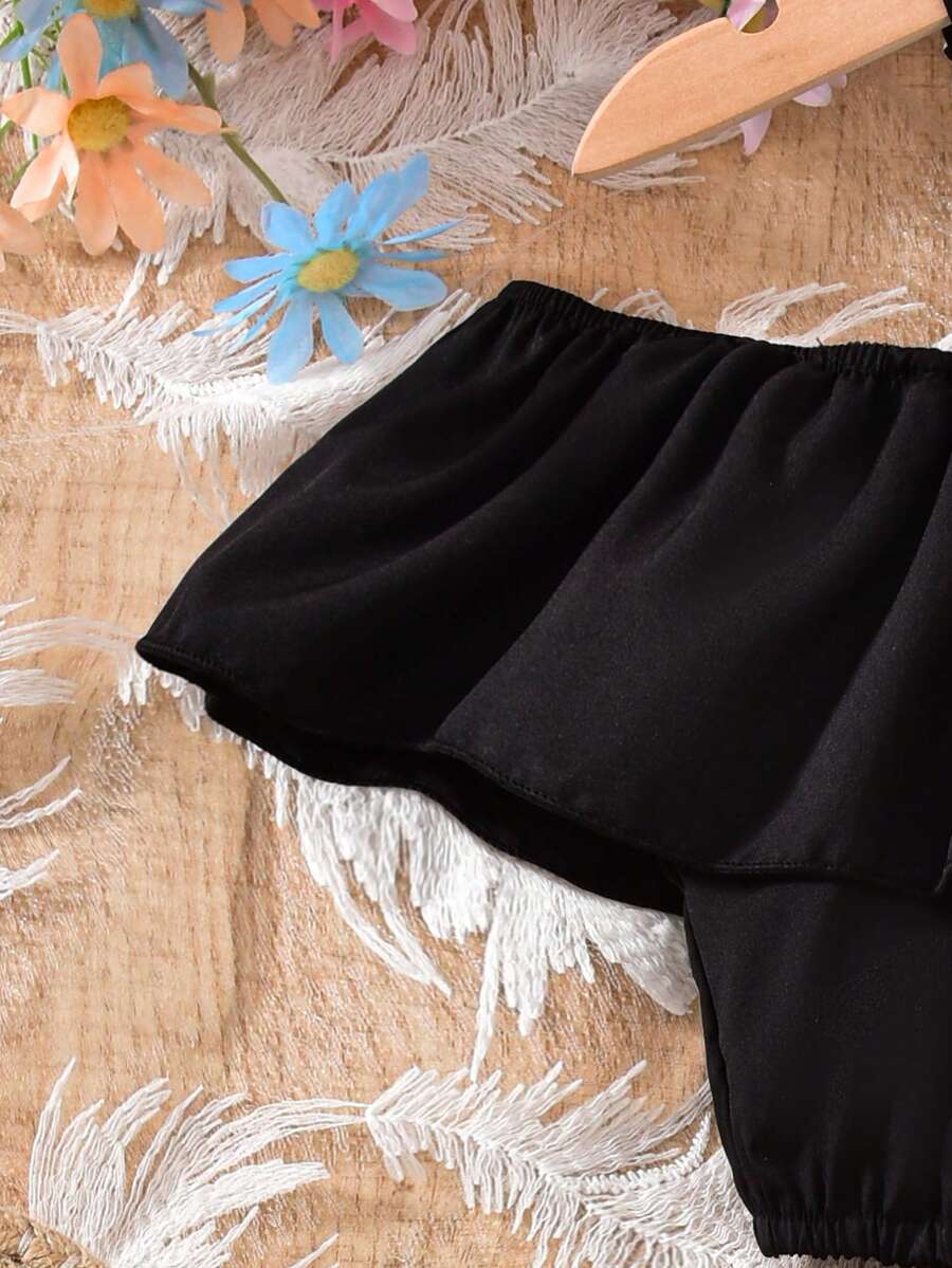 Tween girls 2-piece summer set featuring a black off-shoulder crop top with spaghetti straps and tropical leaf print ruffled paperbag waist shorts with a matching belt.