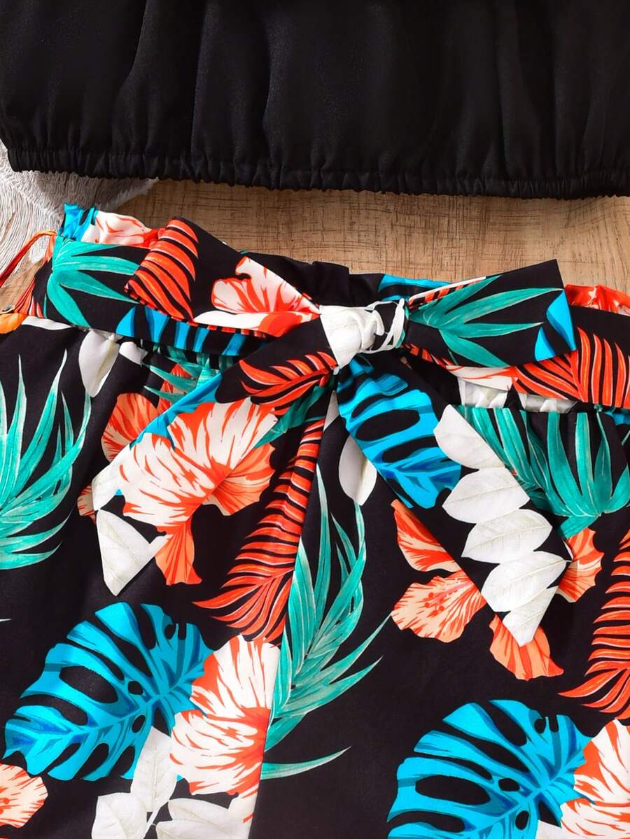 Tween girls 2-piece summer set featuring a black off-shoulder crop top with spaghetti straps and tropical leaf print ruffled paperbag waist shorts with a matching belt.