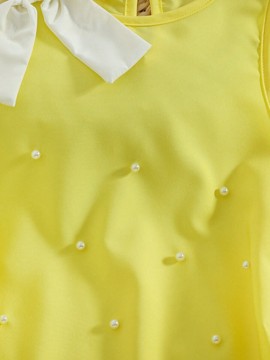 Yellow sleeveless colorblock dress for girls featuring a round neck, ruffle hem, and front bow detail.