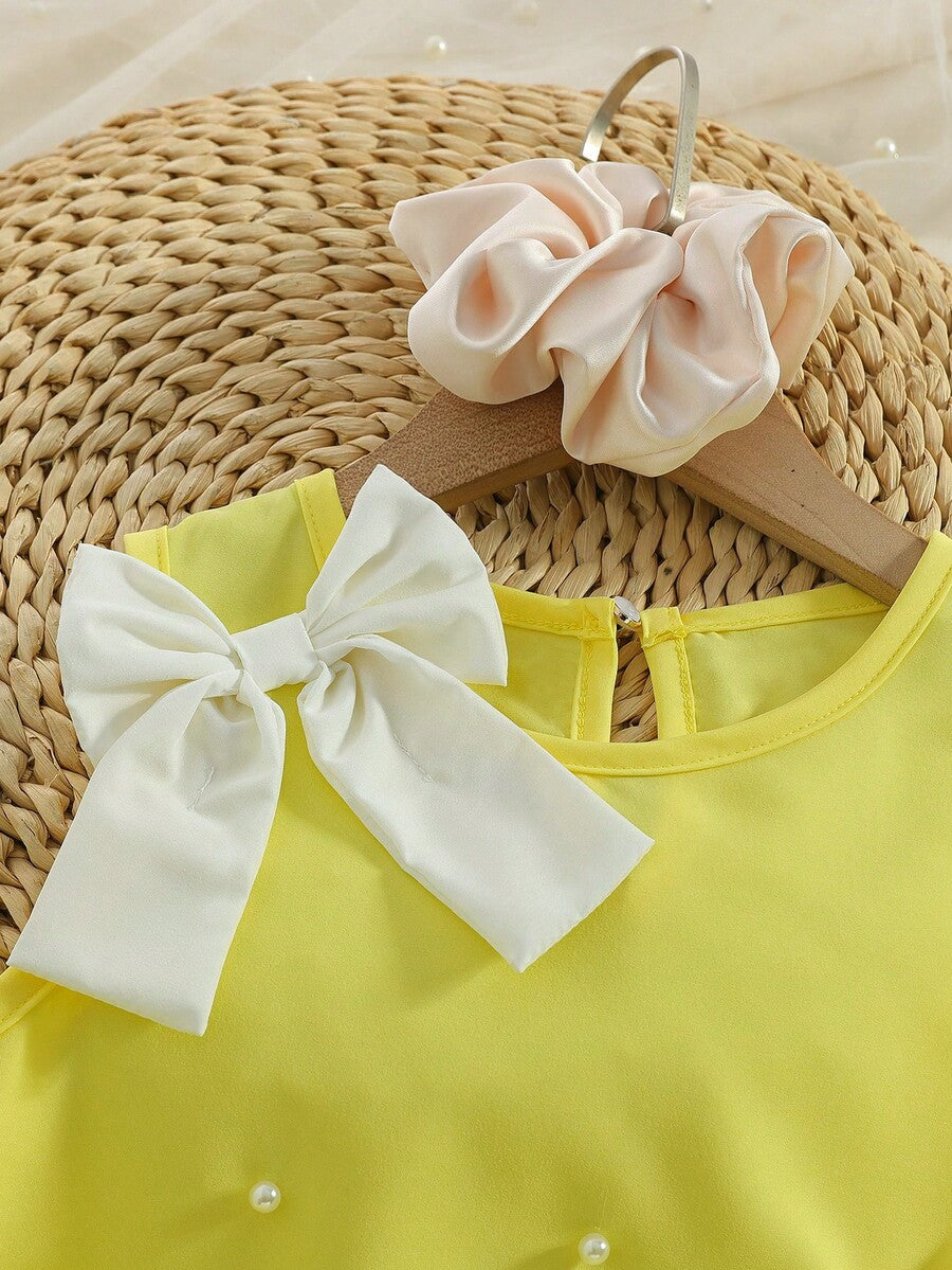 Yellow sleeveless colorblock dress for girls featuring a round neck, ruffle hem, and front bow detail.