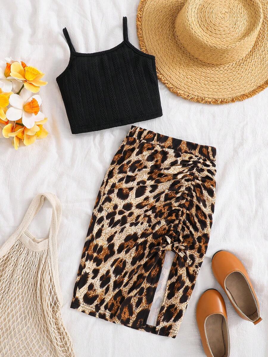 Tween girl wearing a 2-piece set featuring a black rib-knit spaghetti strap camisole top and a ruched leopard print midi skirt.