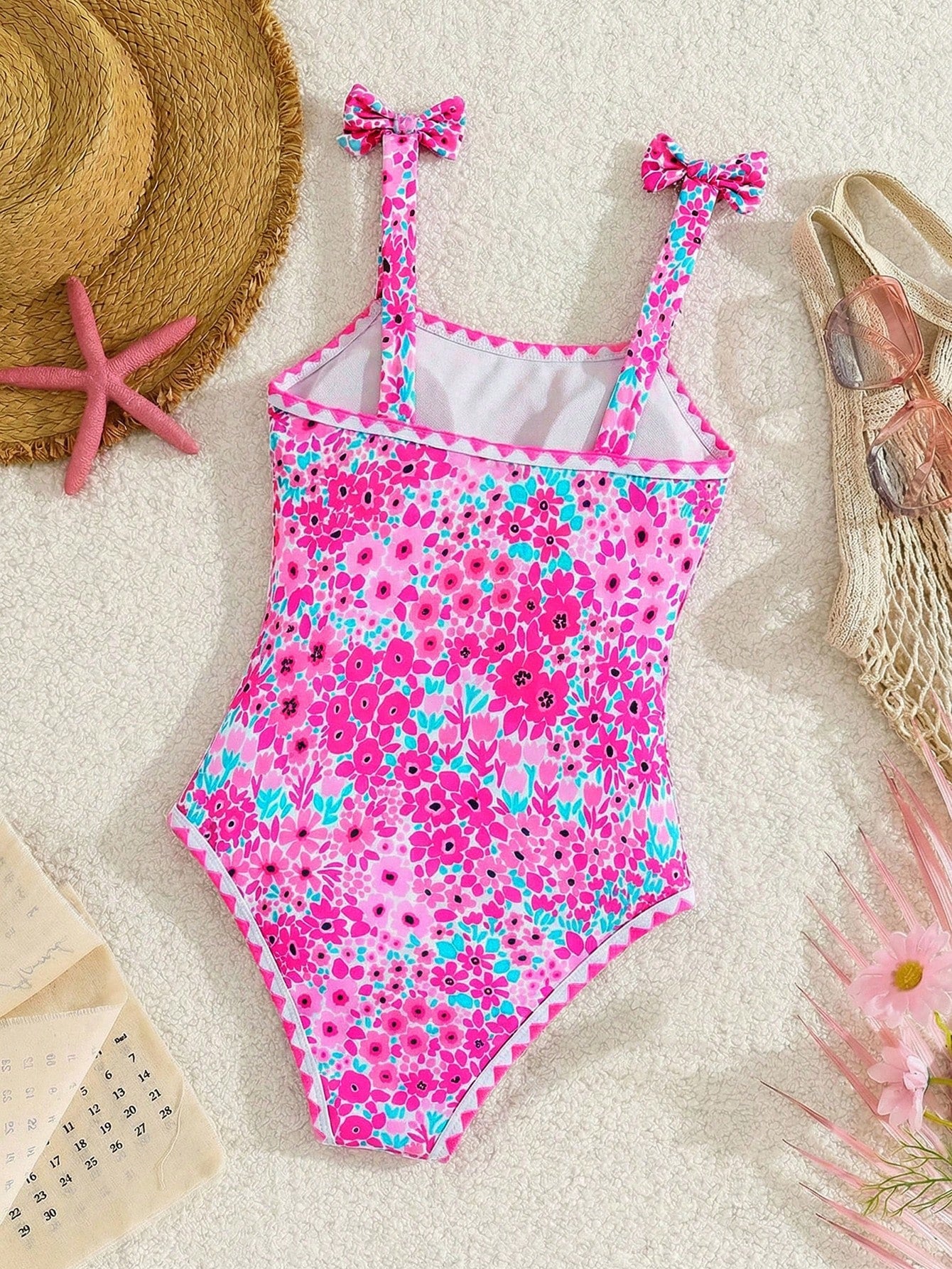 Tween girl floral print one-piece swimsuit with twist front, spaghetti straps, fitted shape, and multicolor all-over hibiscus-inspired pattern for beach and pool wear.