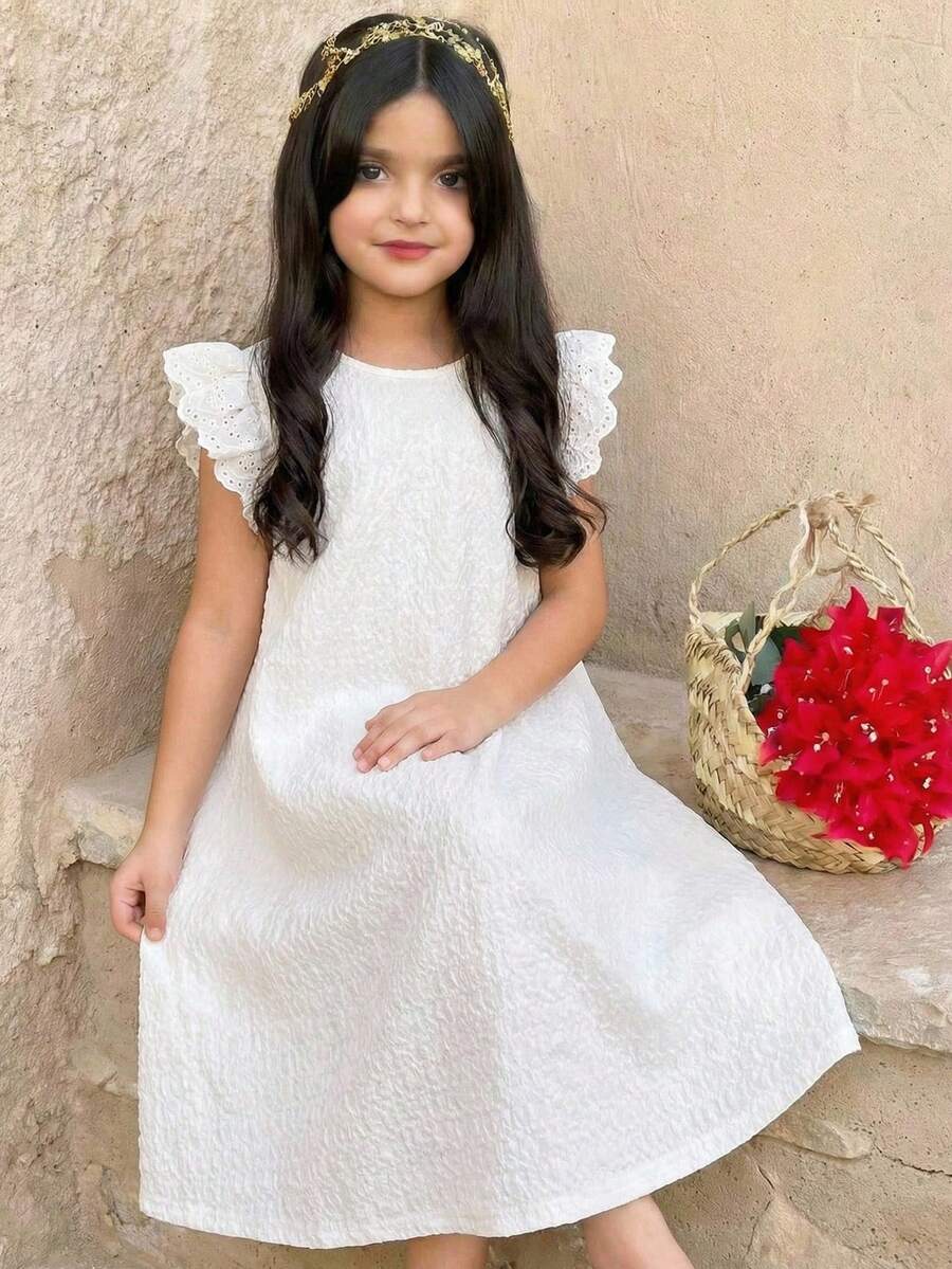 Tween girl wearing a sleeveless black tunic dress featuring a round neck, contrast lace details, and a straight hem.