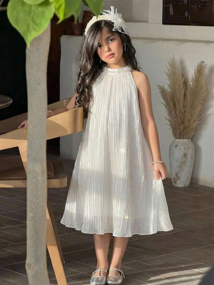 Tween girl wearing a white sleeveless pleated A-line short dress featuring a round neckline and button detail.