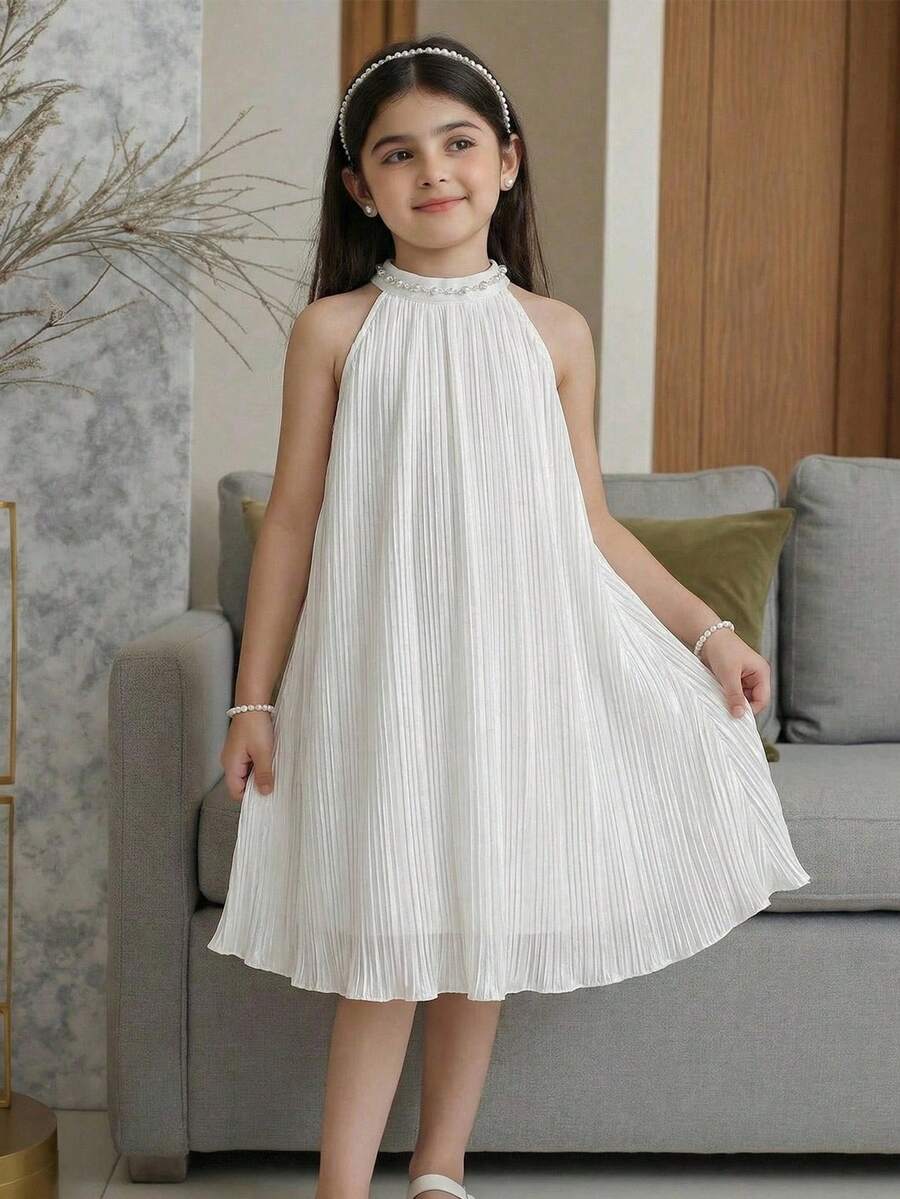Tween girl wearing a white sleeveless pleated A-line short dress featuring a round neckline and button detail.