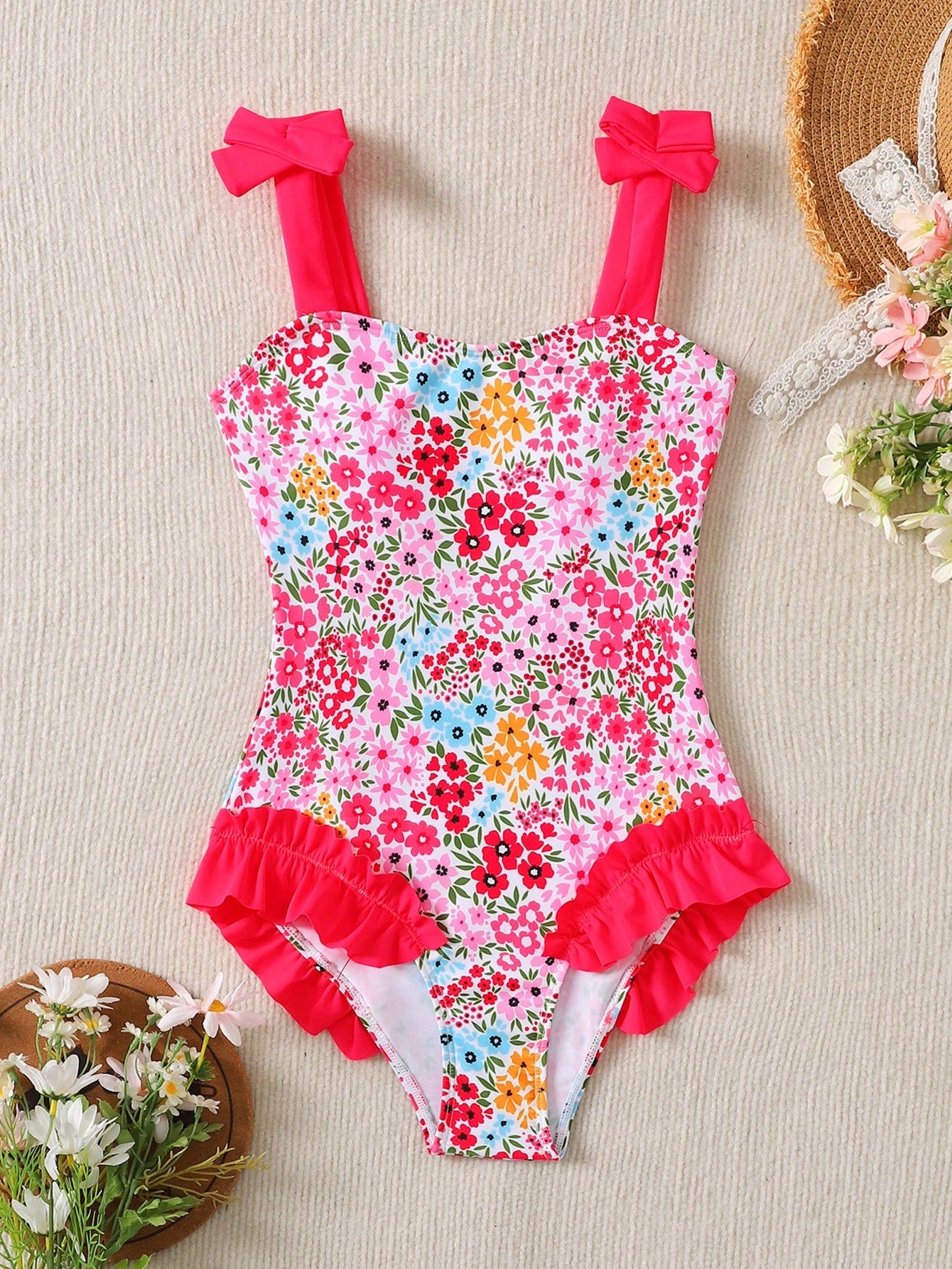 Girls' multicolor one-piece swimsuit with floral plant print, bow detail, asymmetrical ruffle accent, strap neckline, and lined body for beach vacations.