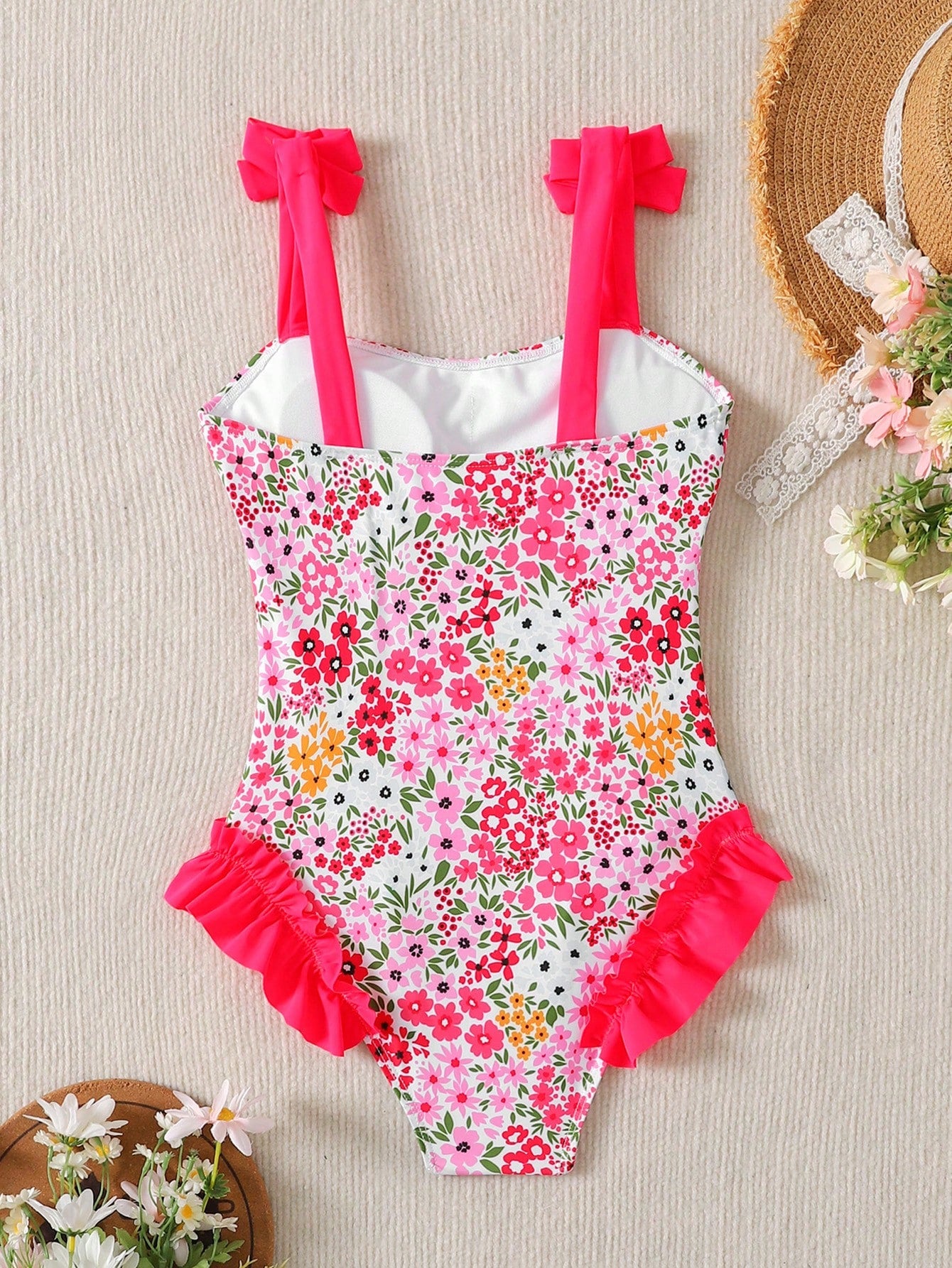 Girls' multicolor one-piece swimsuit with floral plant print, bow detail, asymmetrical ruffle accent, strap neckline, and lined body for beach vacations.