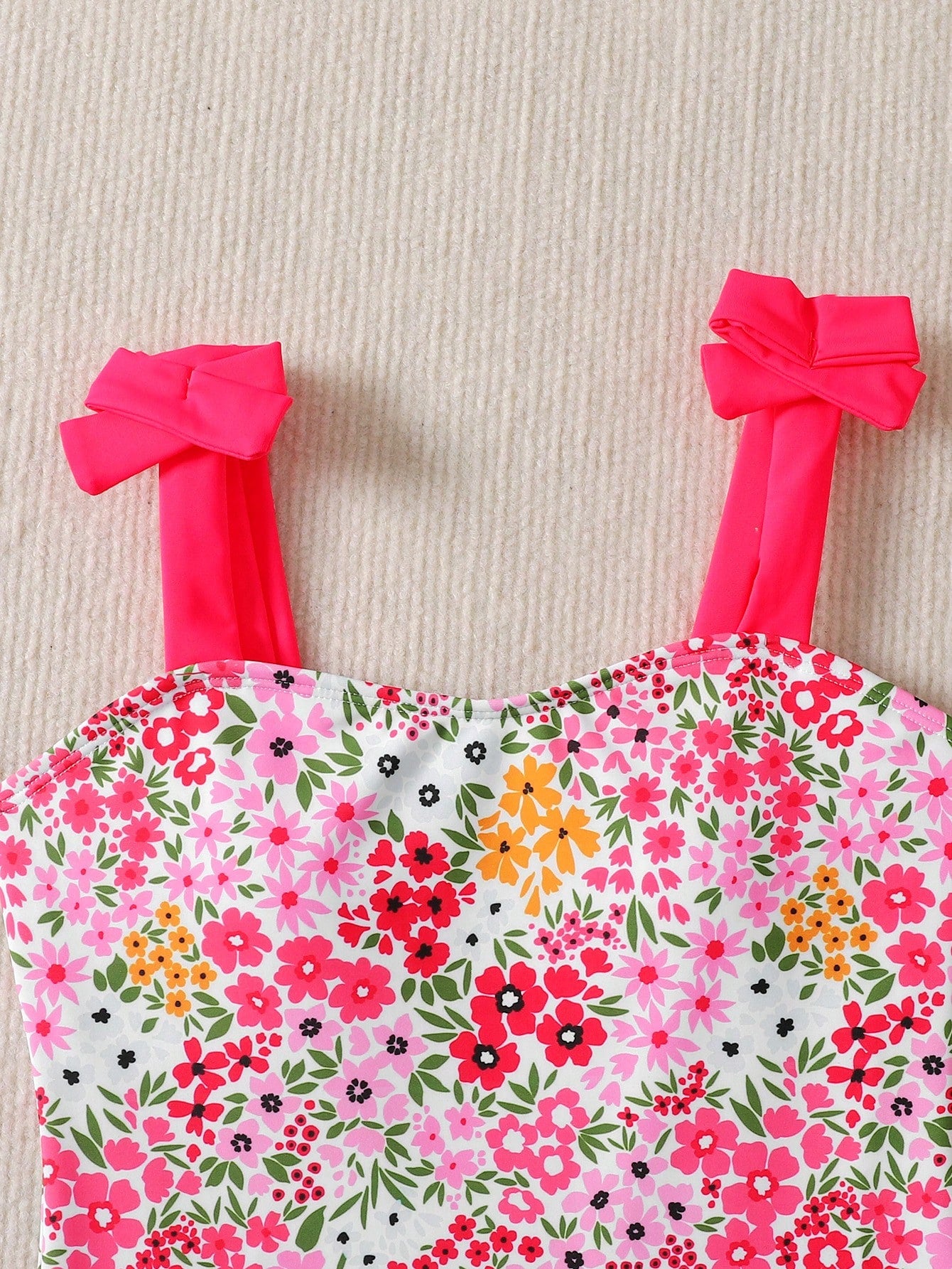 Girls' multicolor one-piece swimsuit with floral plant print, bow detail, asymmetrical ruffle accent, strap neckline, and lined body for beach vacations.