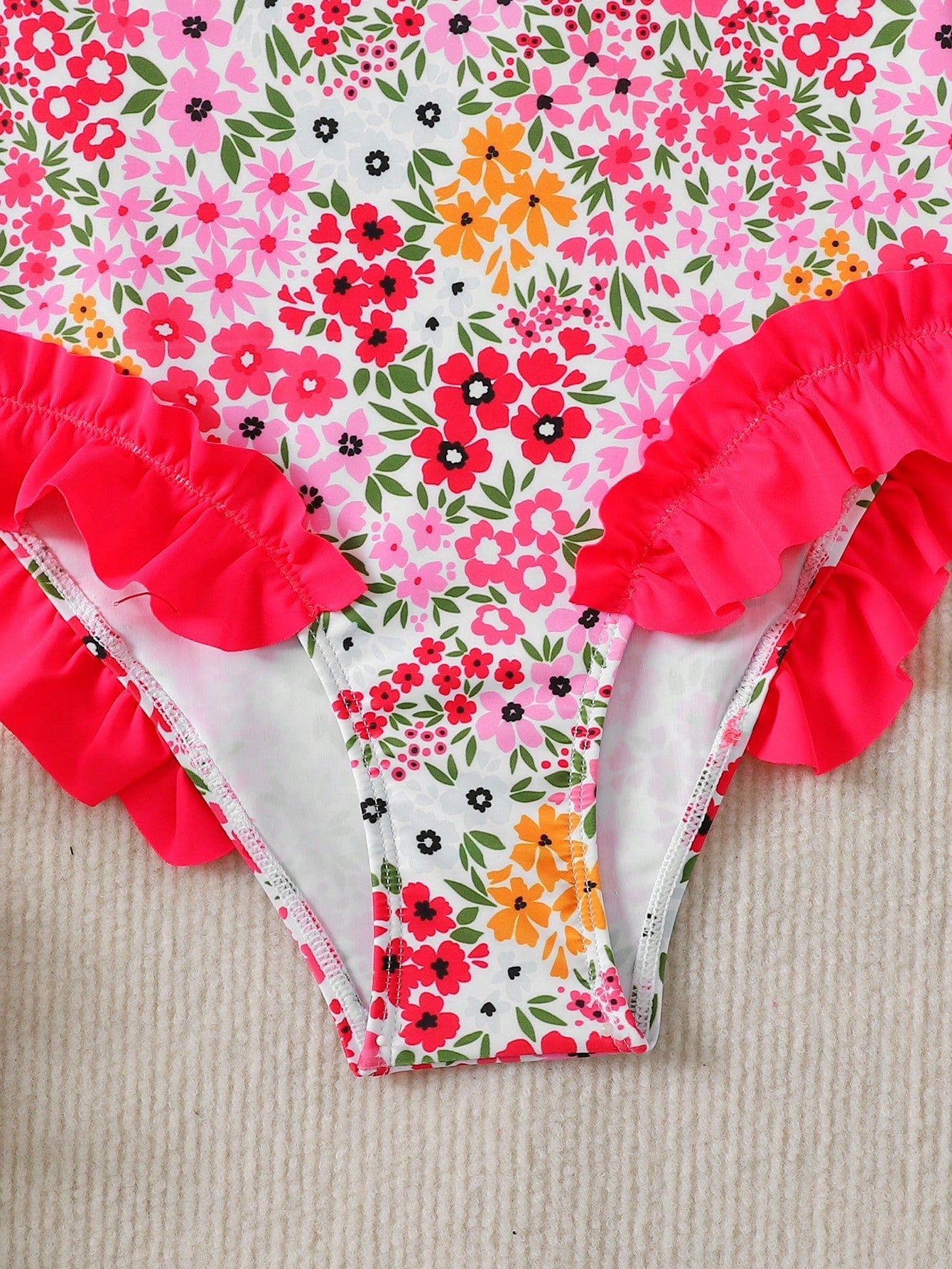 Girls' multicolor one-piece swimsuit with floral plant print, bow detail, asymmetrical ruffle accent, strap neckline, and lined body for beach vacations.