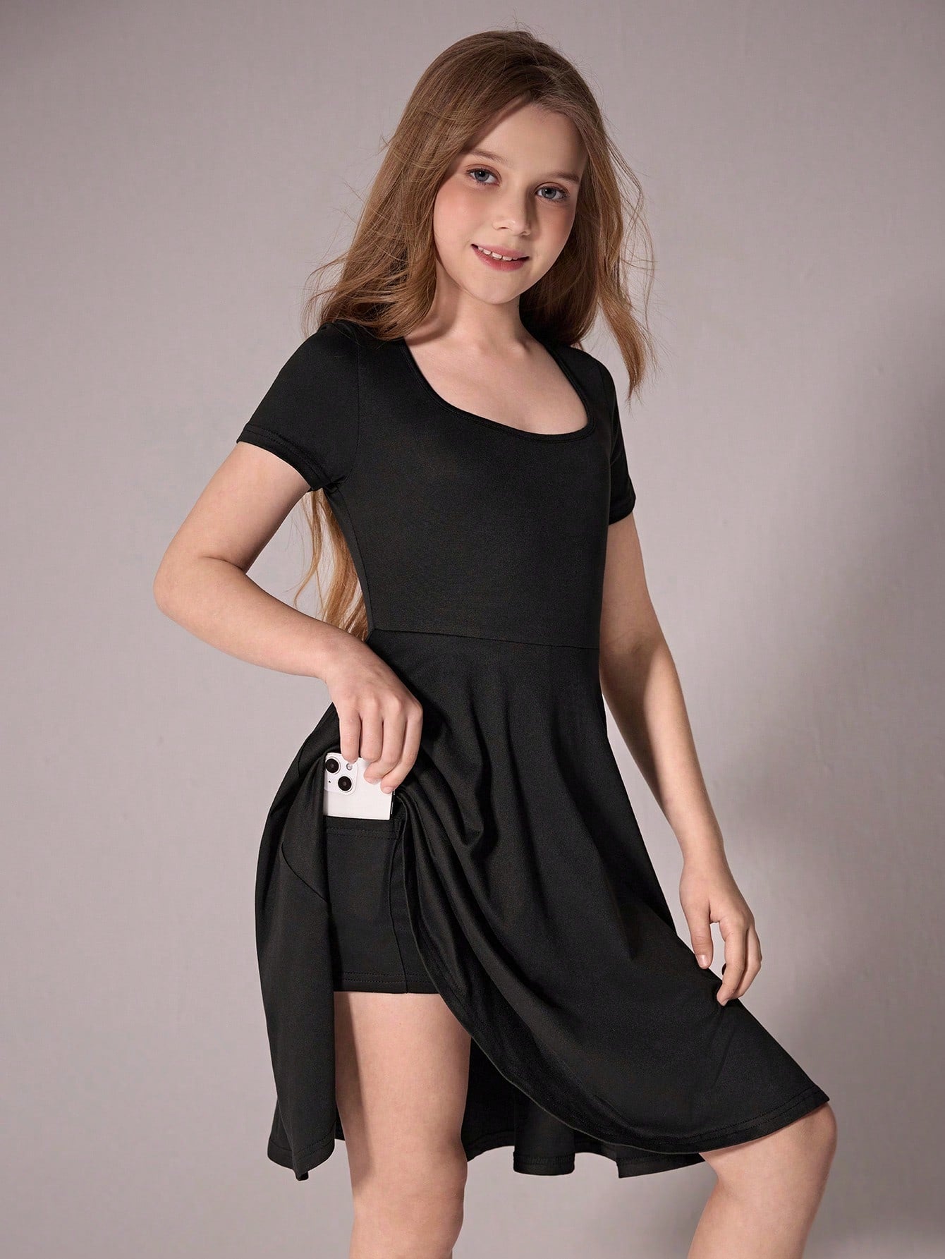 Tween girl wearing a casual black short sleeve knit mini dress with a round neck, high waist, and asymmetrical flared hem