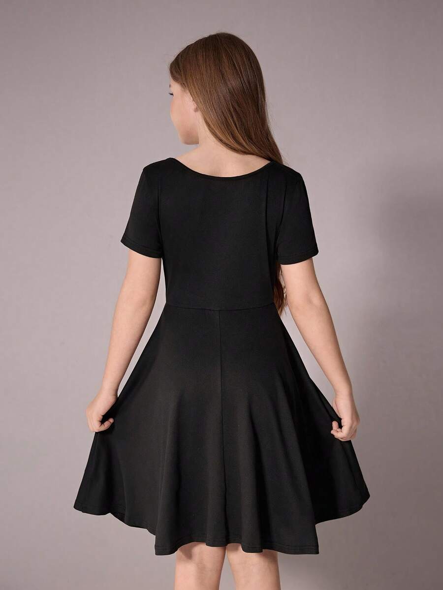 Tween girl wearing a casual black short sleeve knit mini dress with a round neck, high waist, and asymmetrical flared hem