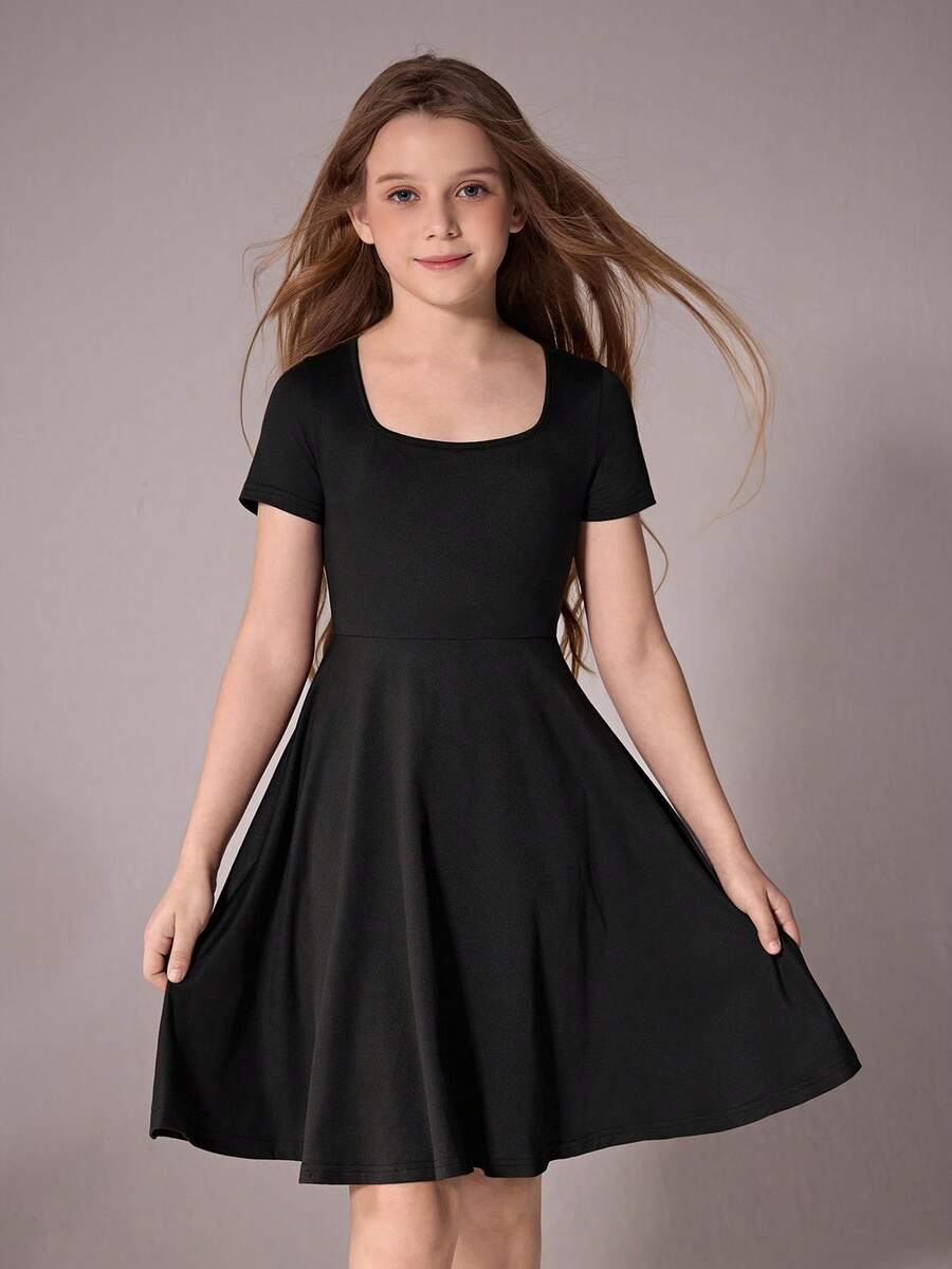 Tween girl wearing a casual black short sleeve knit mini dress with a round neck, high waist, and asymmetrical flared hem