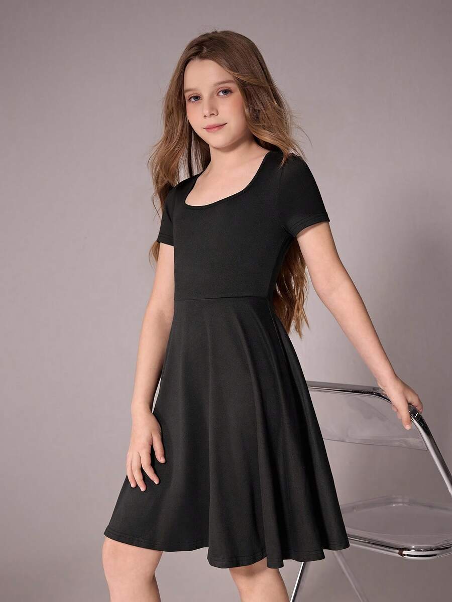 Tween girl wearing a casual black short sleeve knit mini dress with a round neck, high waist, and asymmetrical flared hem