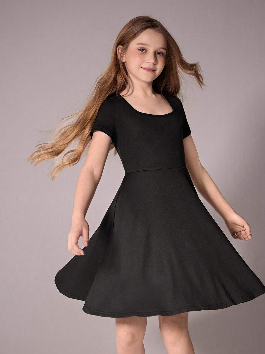Tween girl wearing a casual black short sleeve knit mini dress with a round neck, high waist, and asymmetrical flared hem