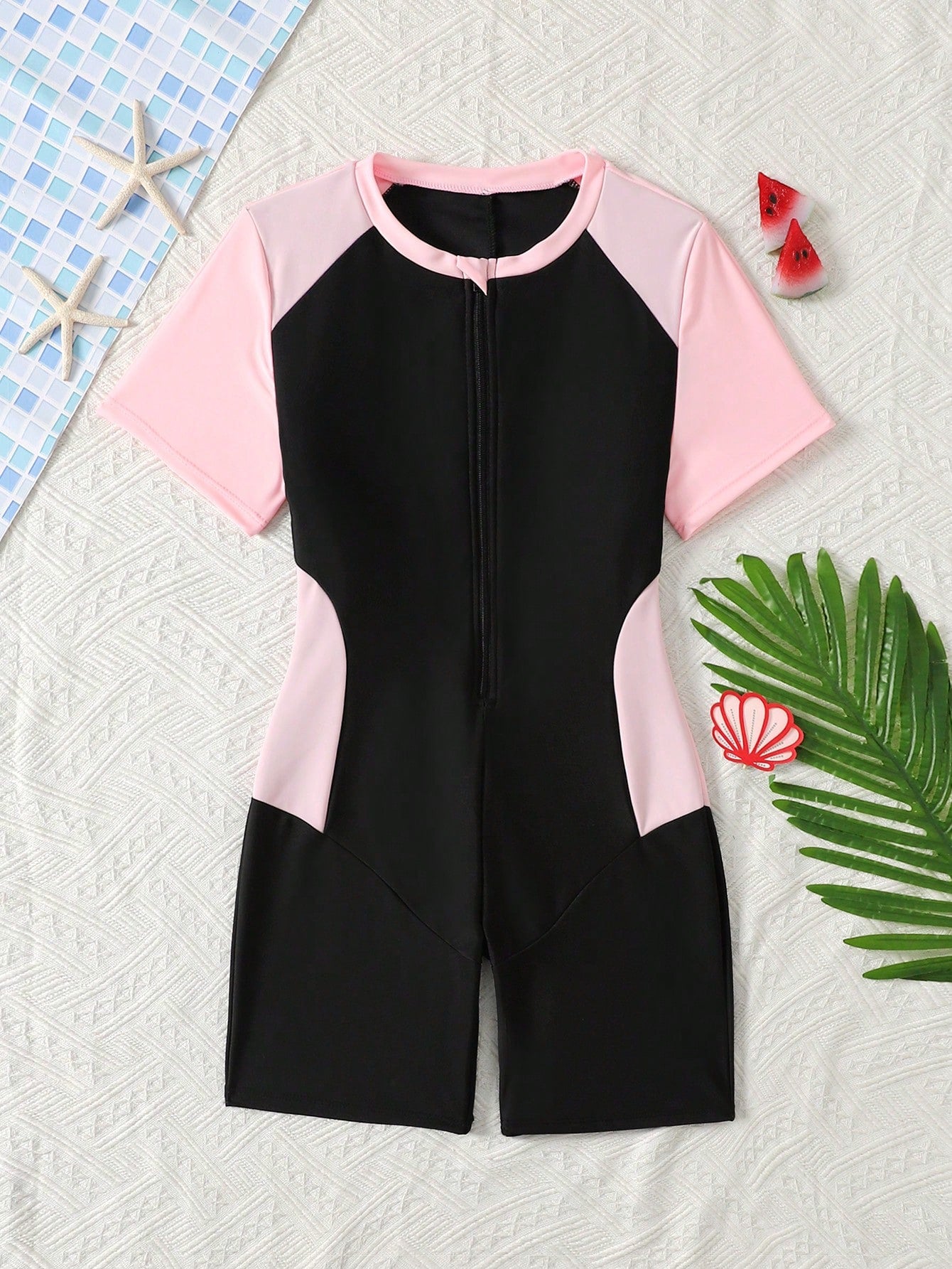 Black and white one-piece rashguard swimsuit for tween girls with short sleeves, high neck, zipper detail, fitted shape, and shorts-style bottom.