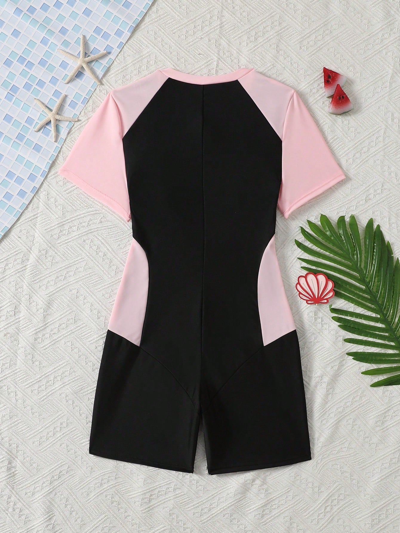 Black and white one-piece rashguard swimsuit for tween girls with short sleeves, high neck, zipper detail, fitted shape, and shorts-style bottom.