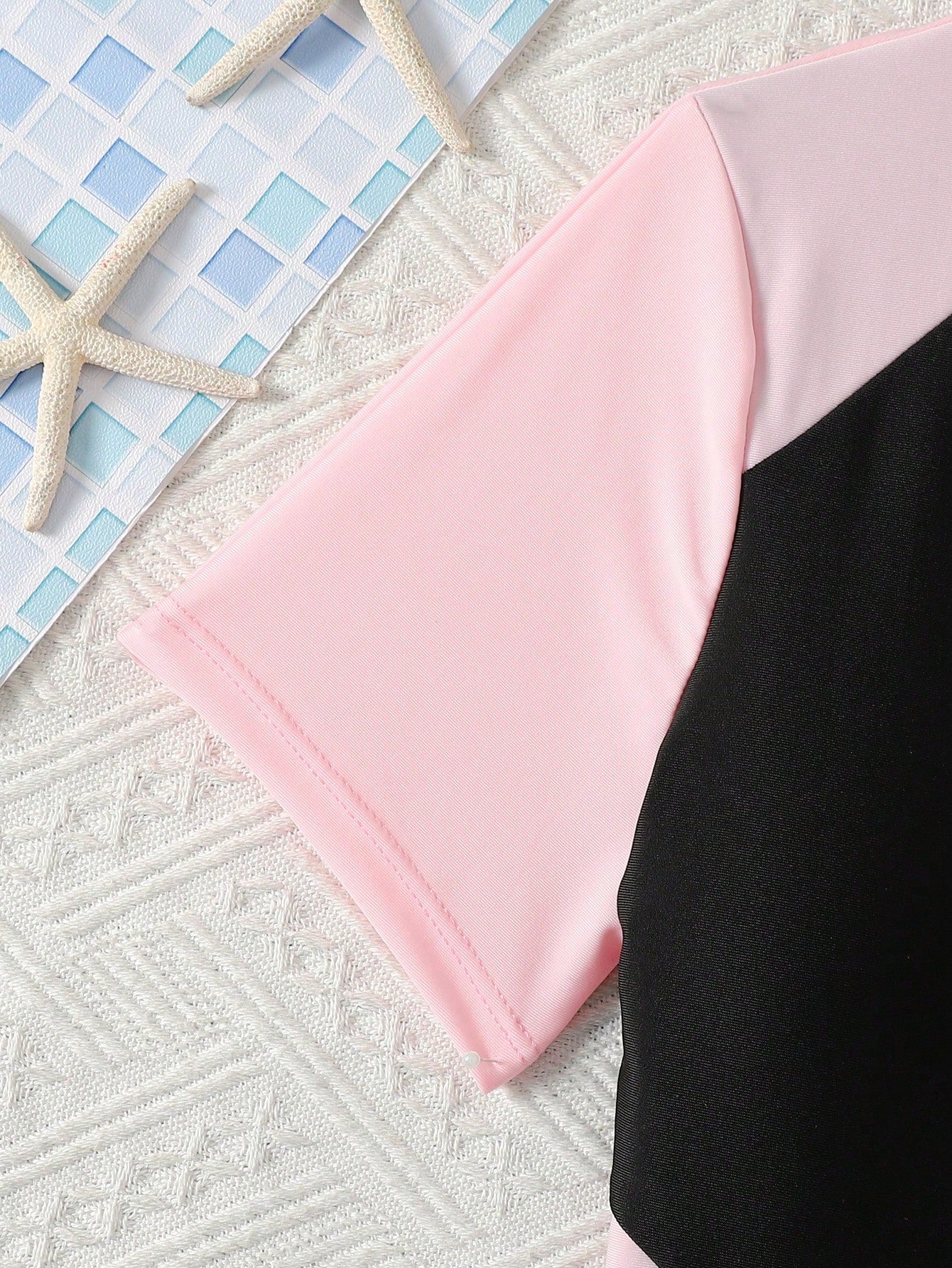 Black and white one-piece rashguard swimsuit for tween girls with short sleeves, high neck, zipper detail, fitted shape, and shorts-style bottom.